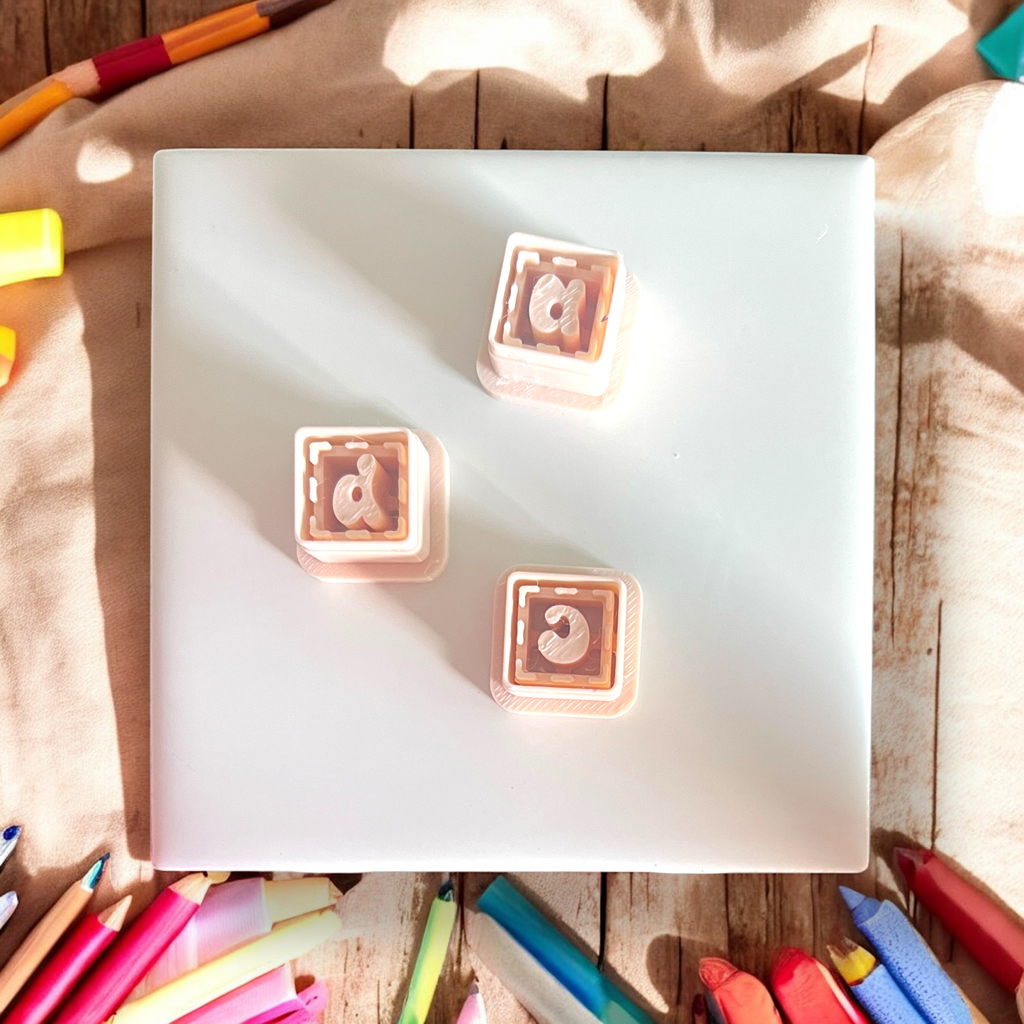 Two square letter stamps on a white surface with colorful markers around.