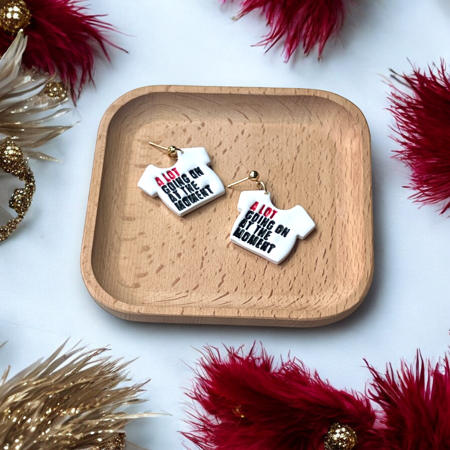 Statement earrings with "A Lot Going On at the Moment" in bold red and black, displayed on a wooden plate on table.