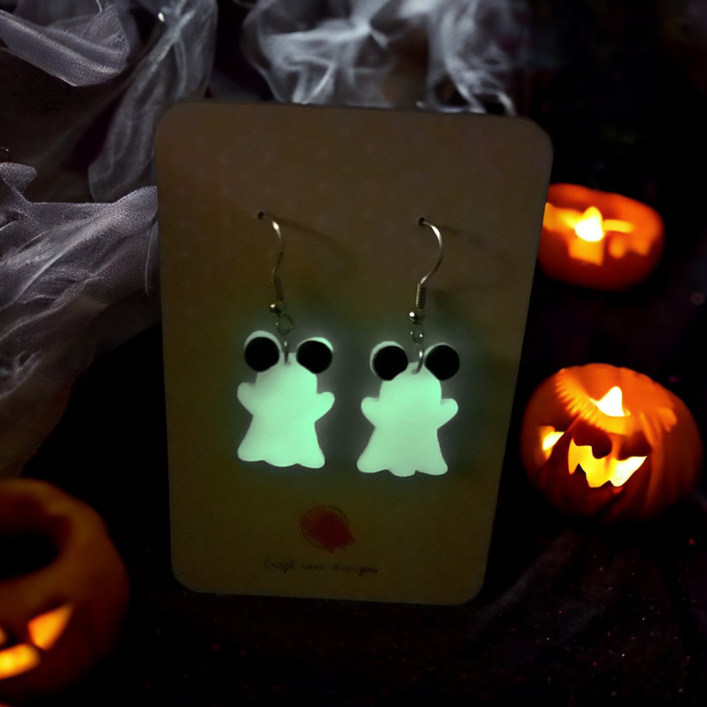 Glow-in-the-dark mouse ghost earrings with black ears, photographed glowing in dim light, creating a fun and spooky aesthetic.