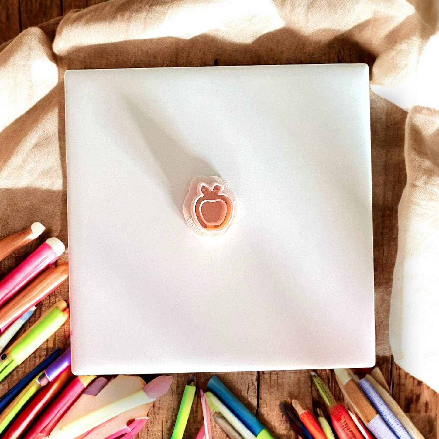 Top view of a layered apple-shaped clay cutter resting alone in the center of a square tile.
