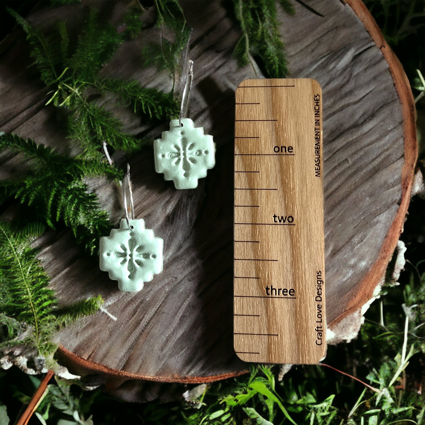 Mint green Aztec dangle hoop earrings with intricate detailing, shown next to a wooden ruler in a natural outdoor setting.