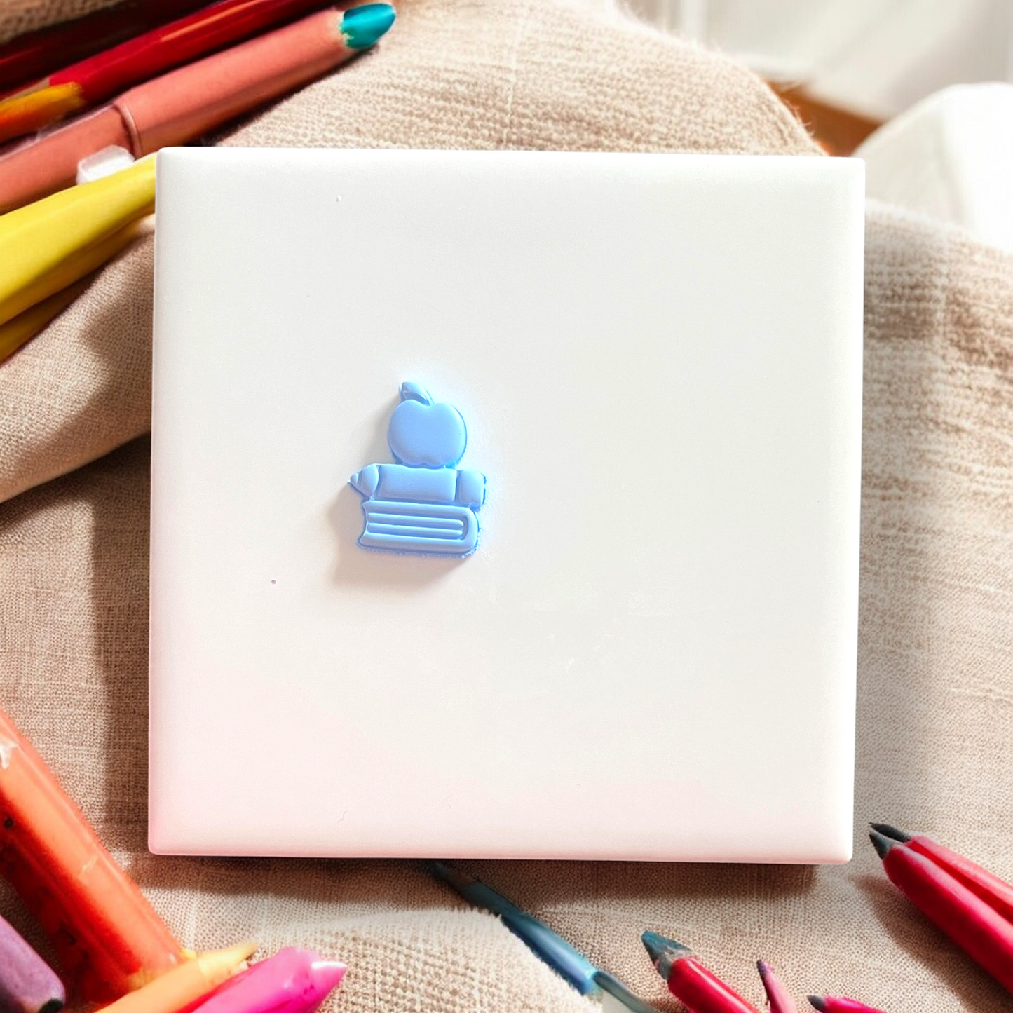 White notebook with a blue eraser on top, surrounded by colorful markers on a beige fabric background