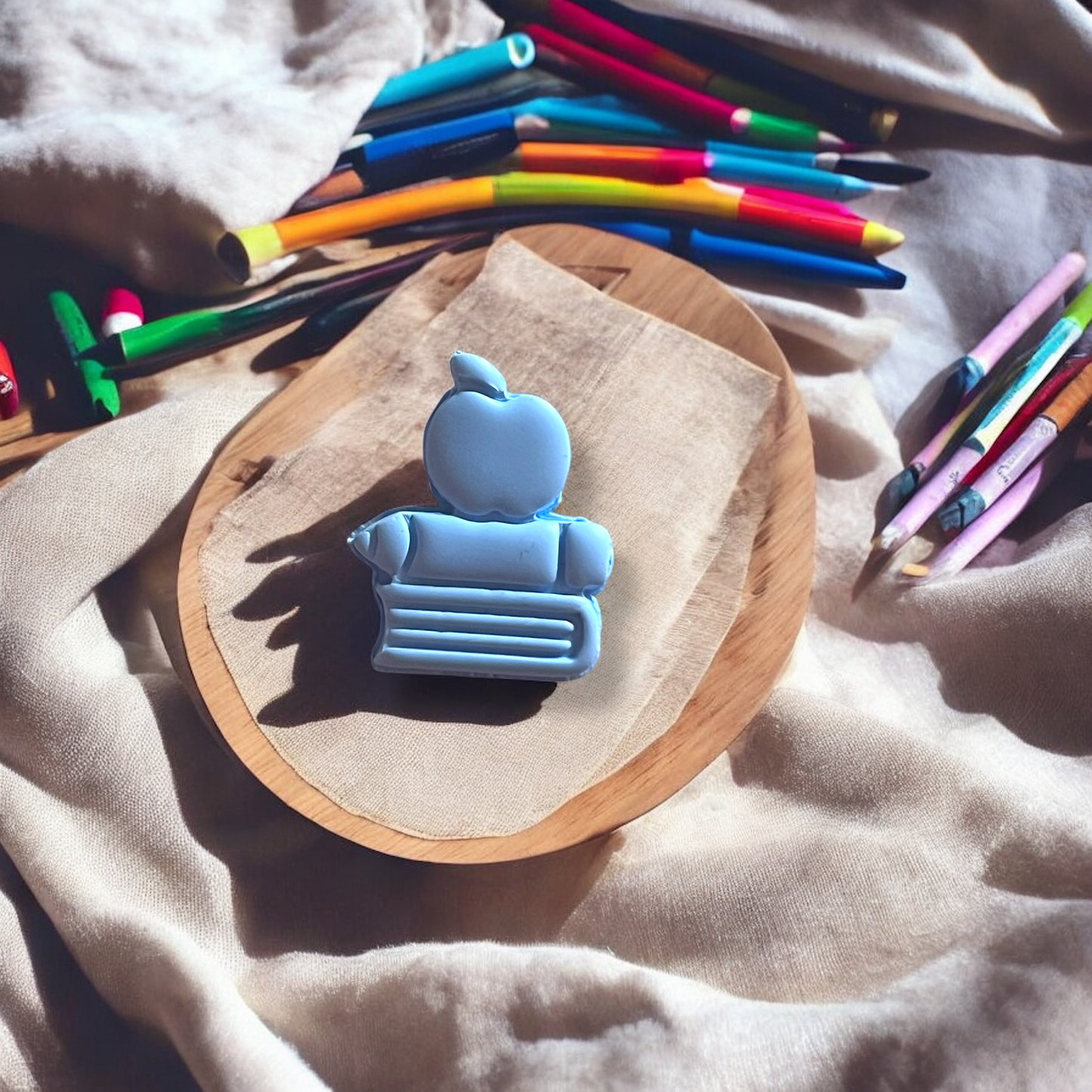 Blue robot-shaped eraser on a wooden block with colorful pencils in the background.
