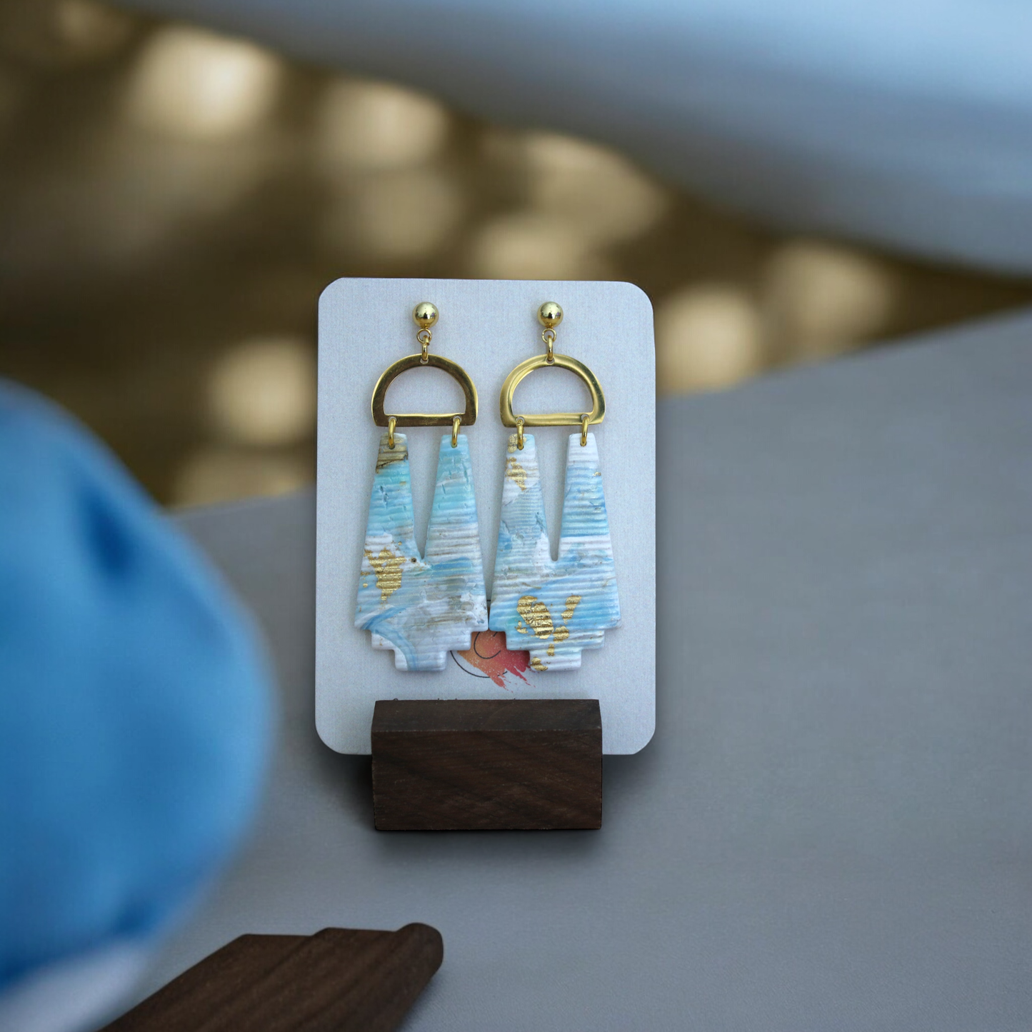 Beachy marbled earrings featuring blue, beige, and gold details, shown on a textured woven background for a natural, coastal vibe.