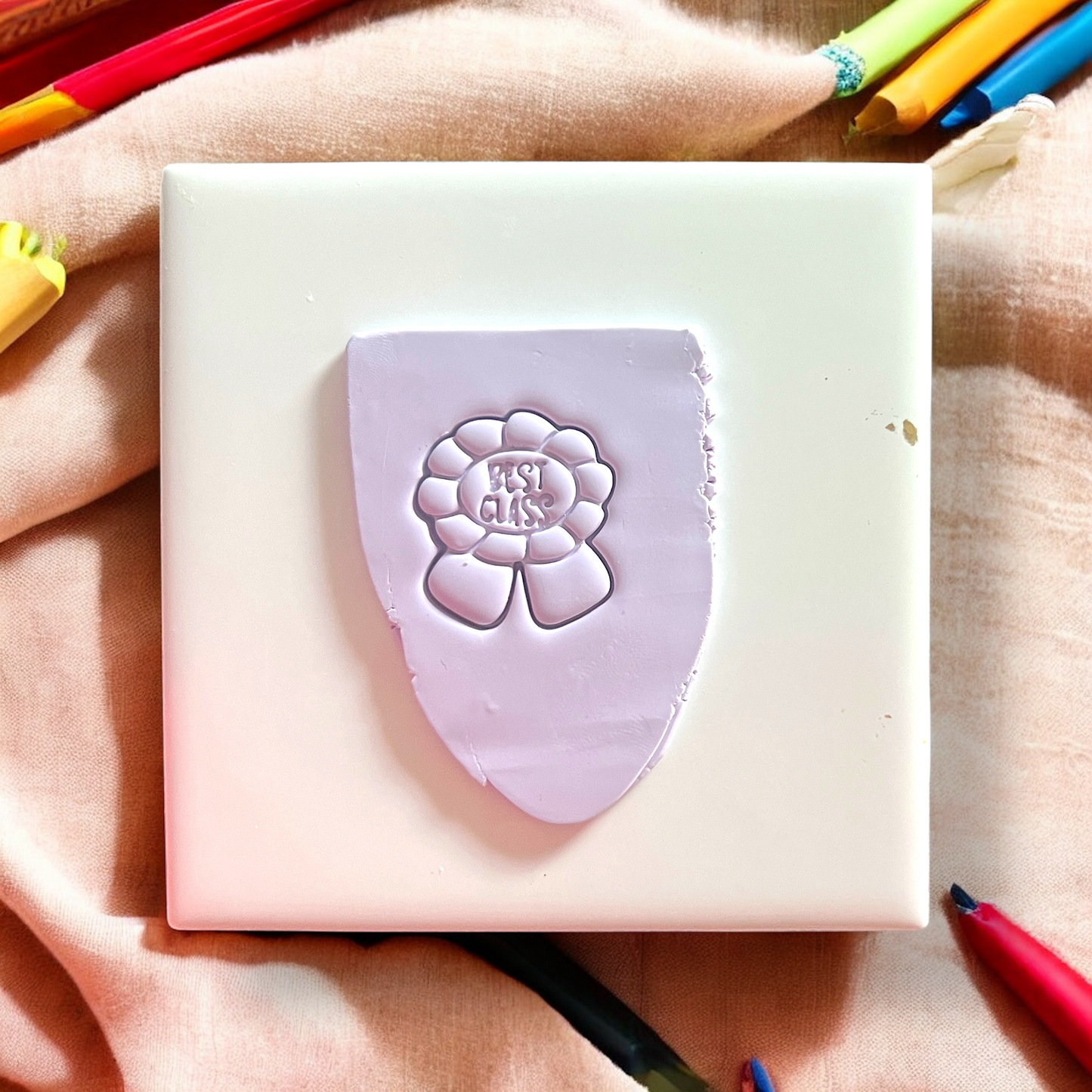 Purple flower-shaped stamp on a white block with colorful pencils in the background