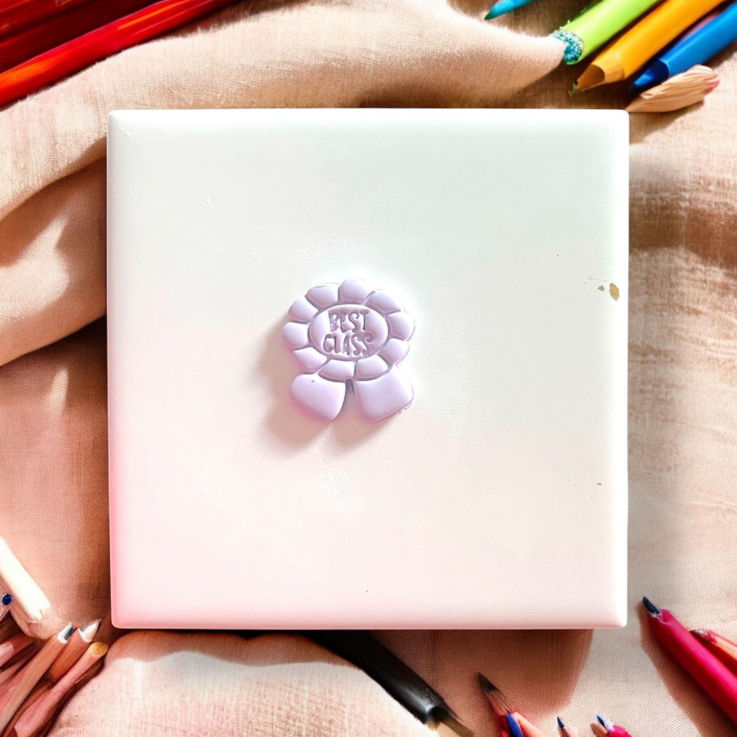 Pink notebook with a purple flower-shaped sticker on top, surrounded by colorful pencils.