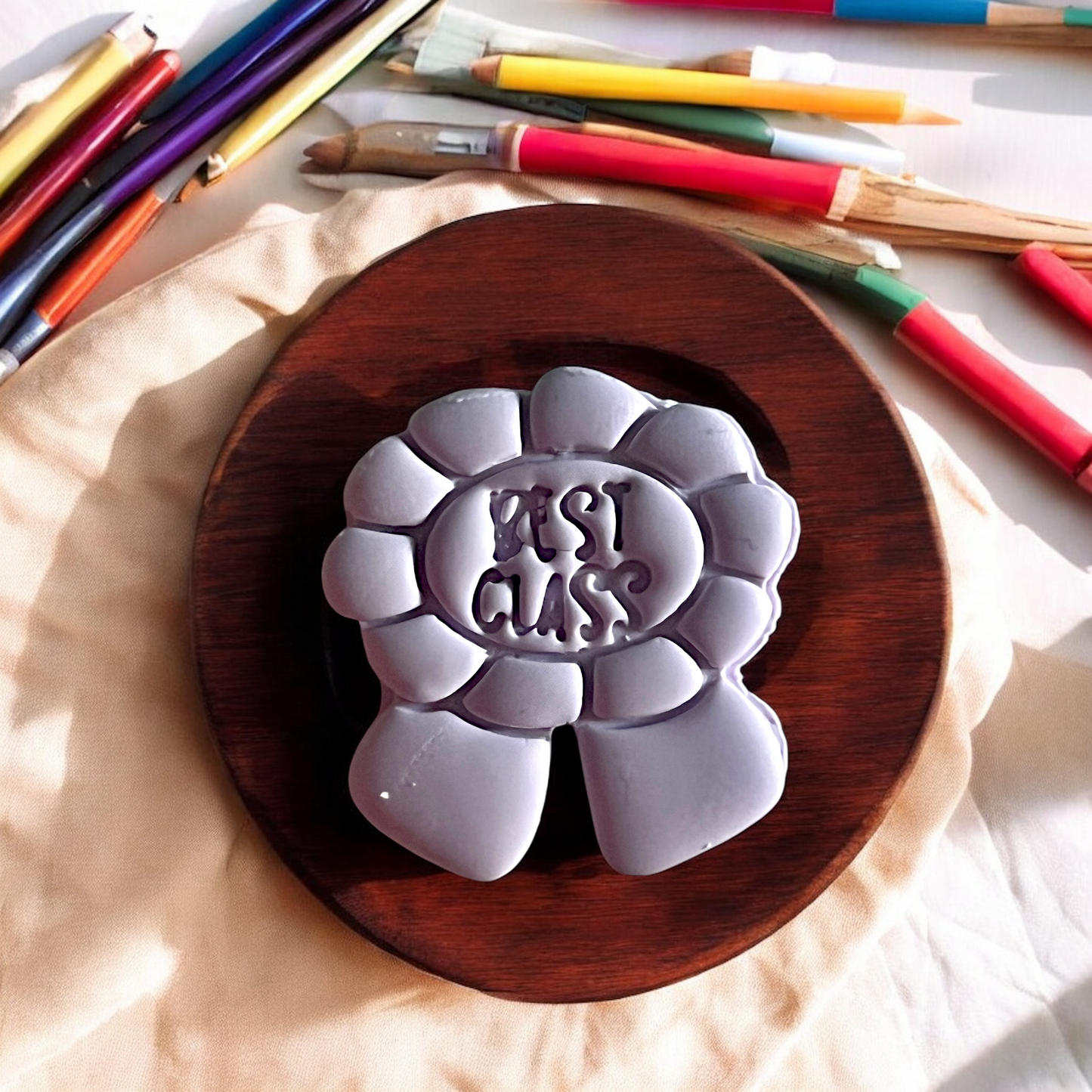 Gray clay mold with 'Moshi Moshi' text on a wooden board, surrounded by art supplies.