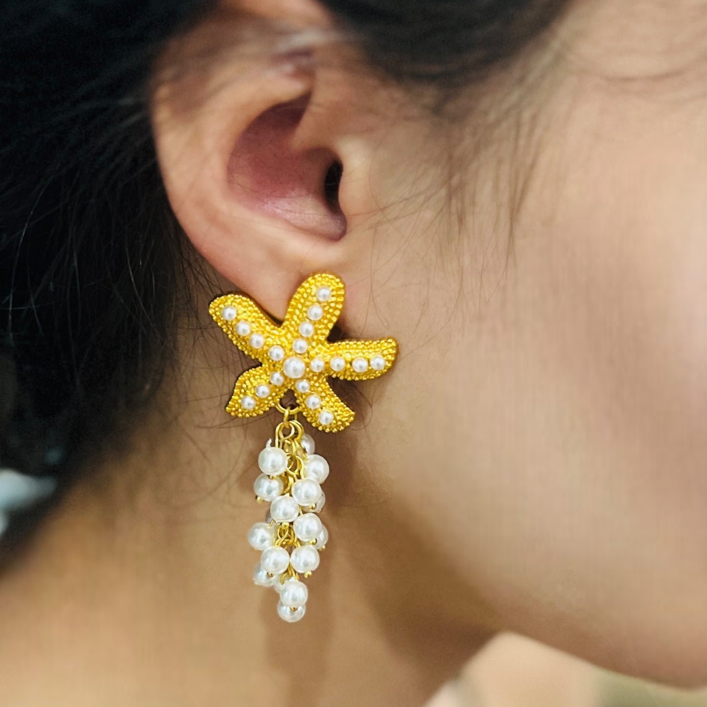 Close-up of boho starfish drop earrings with a gold beaded sea star design and pearl clusters, worn to highlight their boho-chic appeal.
