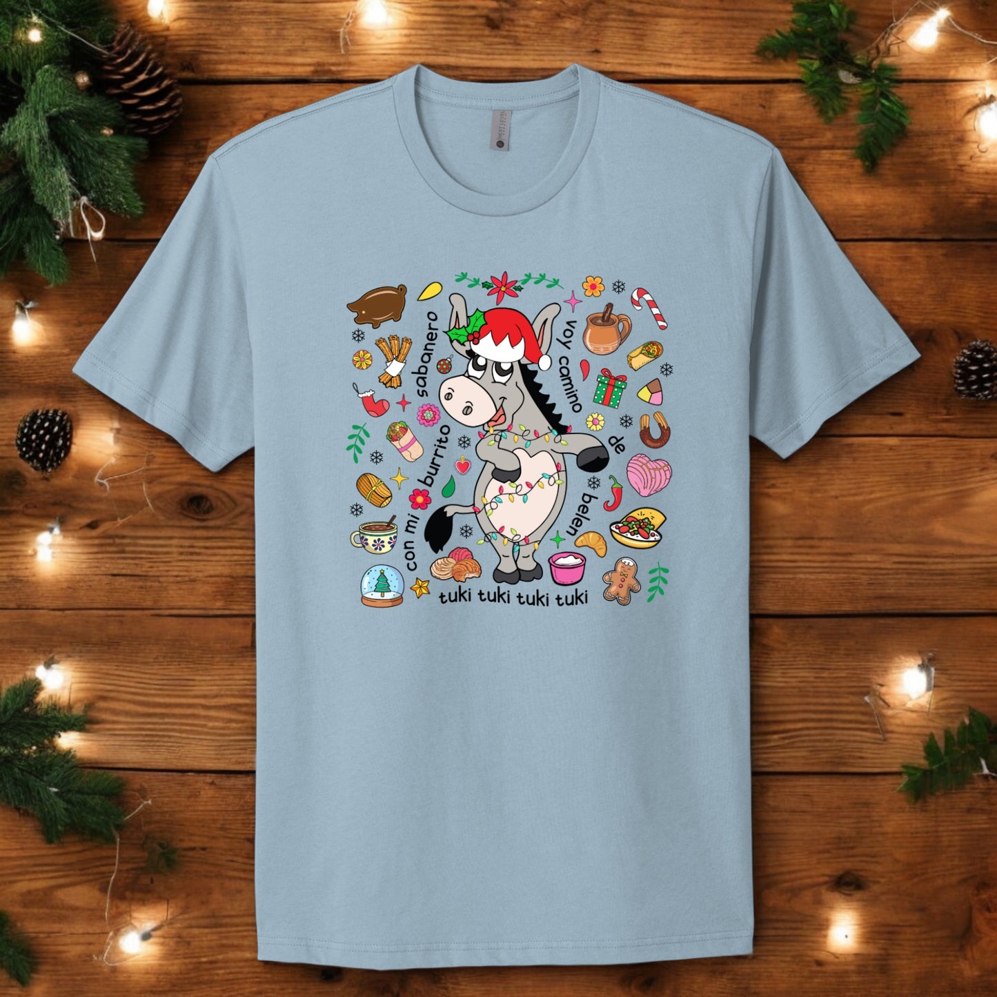 Flat lay of light blue "Burrito Sabanero" holiday t-shirt featuring festive illustrations and lyrics, perfect for Christmas vibes.