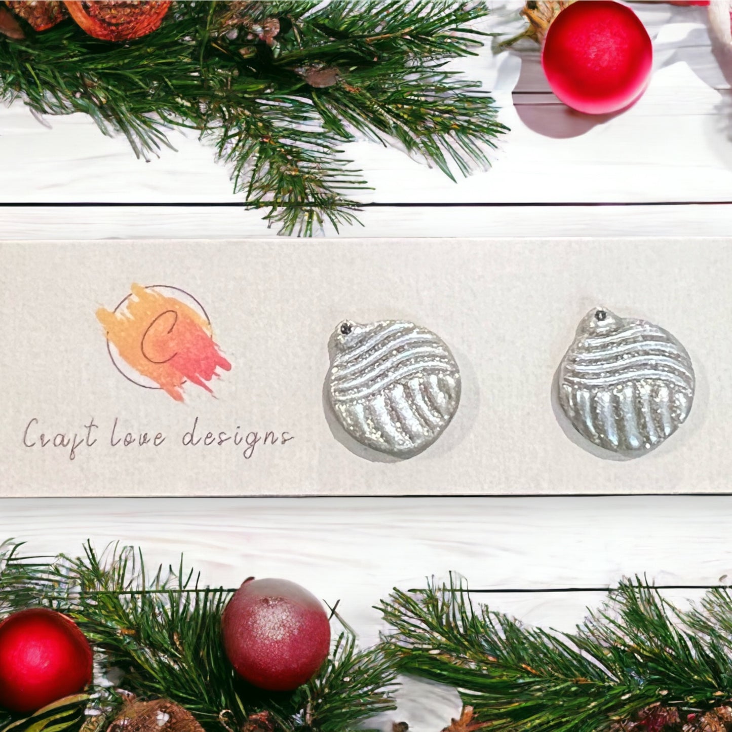 Sparkly silver ornament stud earrings displayed on a festive backdrop, featuring textured designs and surrounded by Christmas greenery decor.