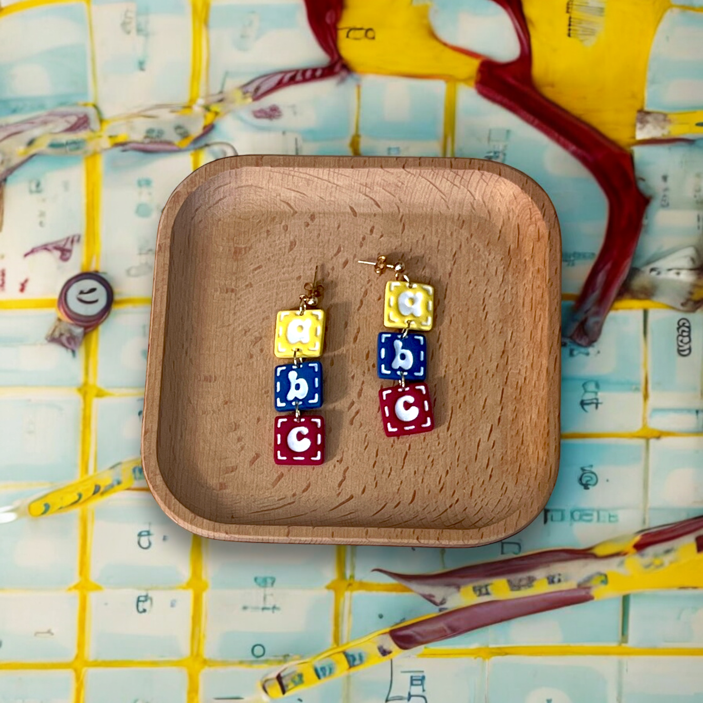 Fun alphabet block earrings with letters A, B, and C, displayed on a wooden tray, perfect for adding a pop of color to your outfit.