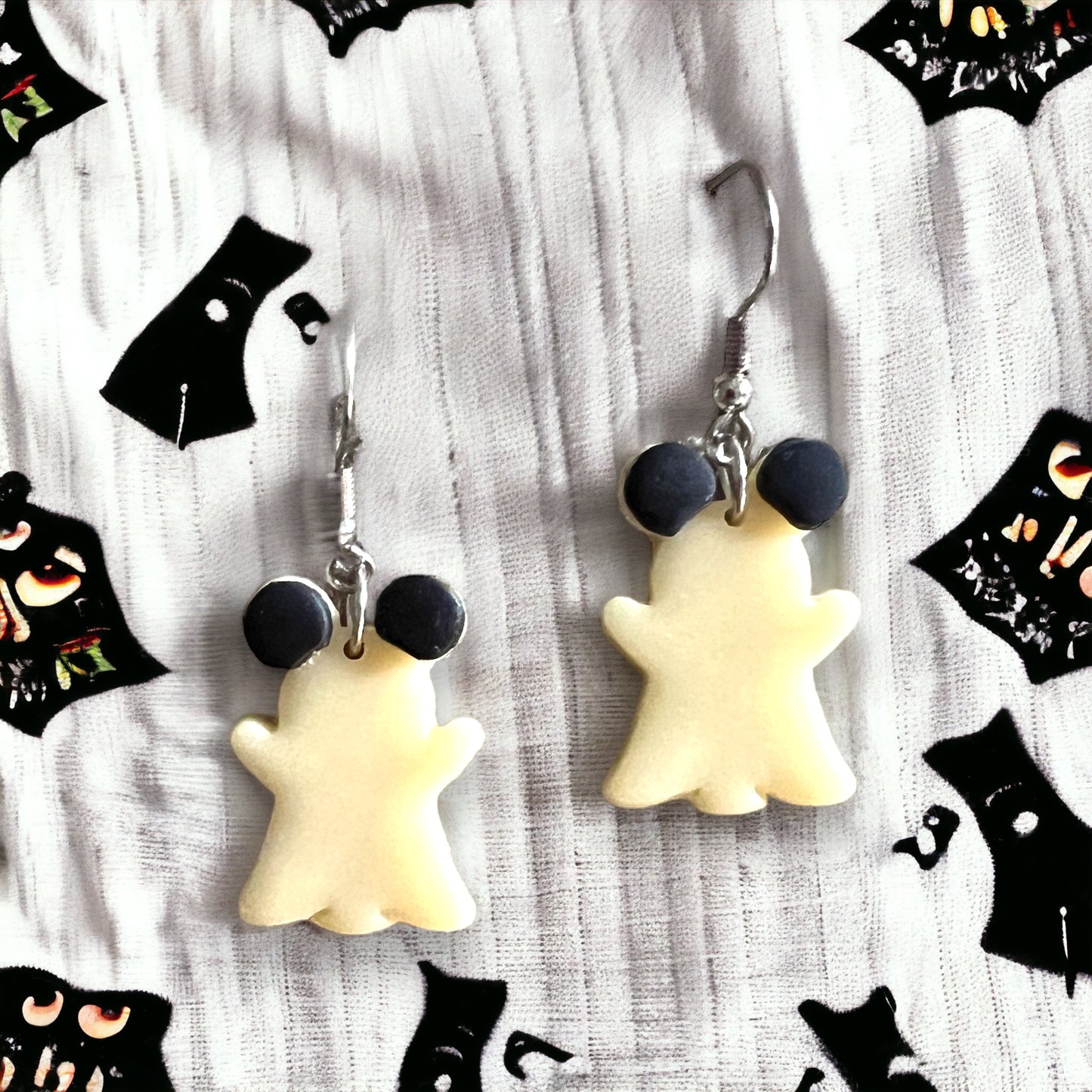 White, glow-in-the-dark dangle earrings shaped like playful ghost mice with black ears, shown on an earring card for Halloween charm.