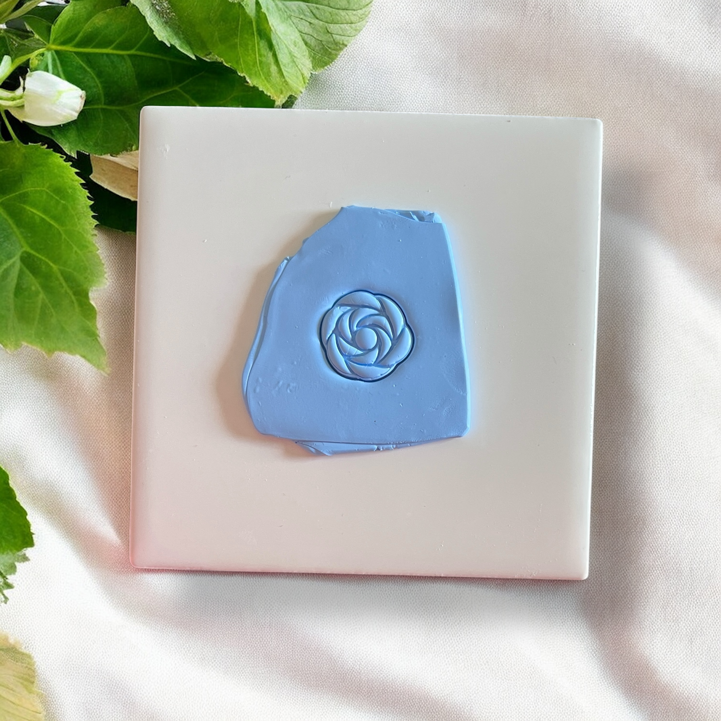 blue clay slab with rose-shaped impression on white tile with greenery