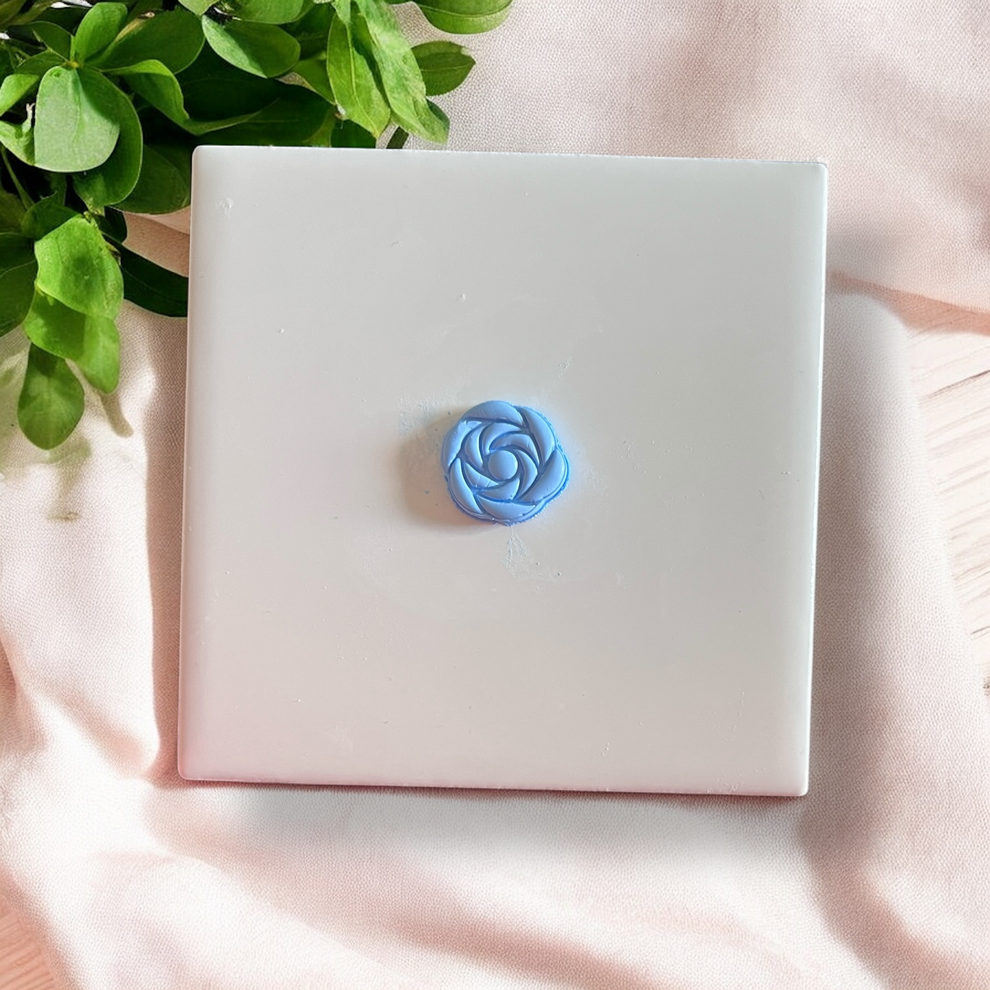 small blue polymer clay rose impression centered on white ceramic tile