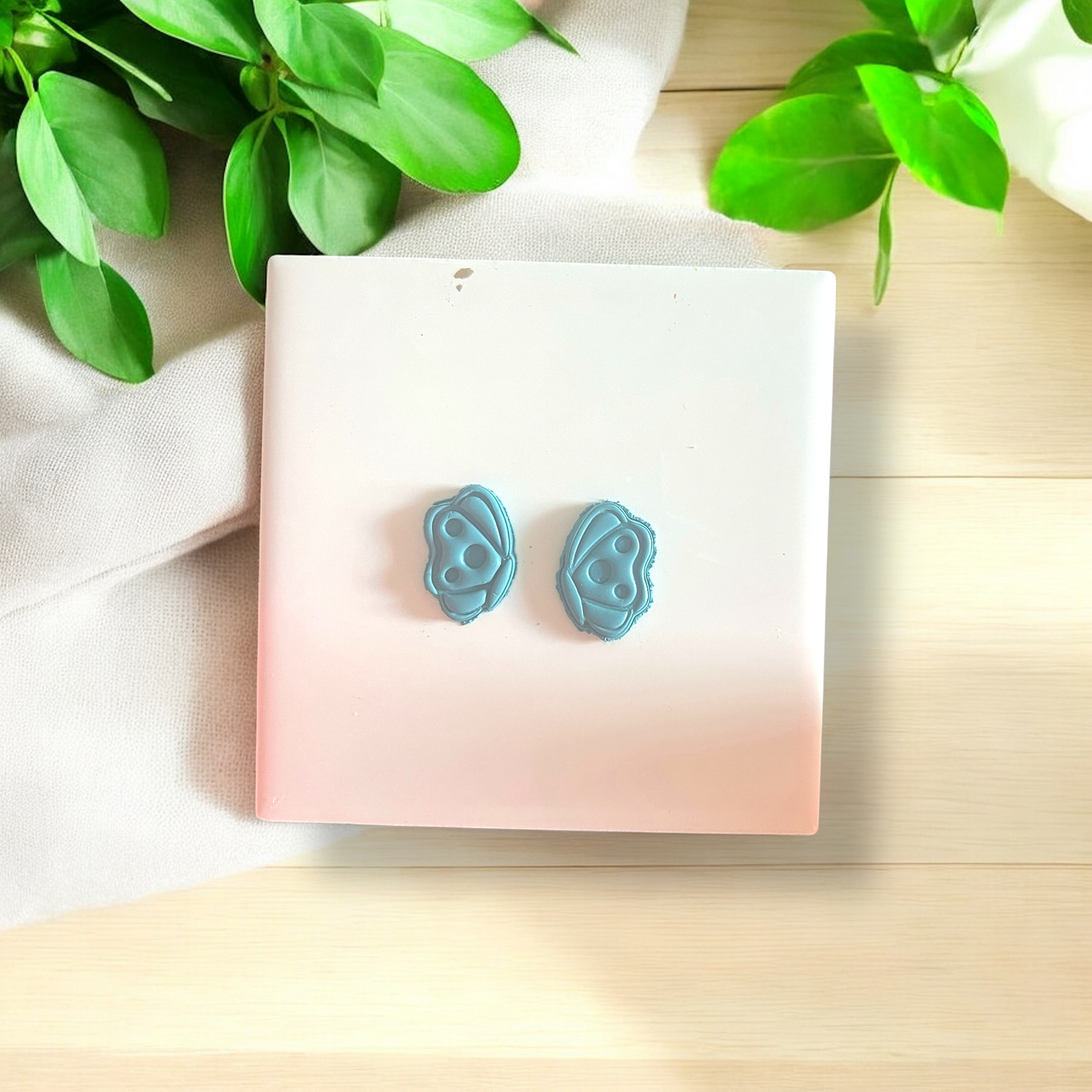 Pair of blue earrings on a pink card with green leaves in the background