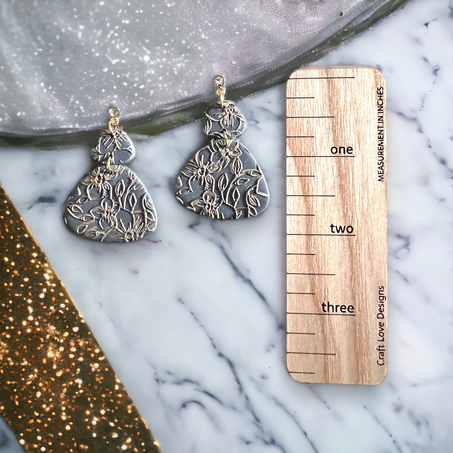 Handcrafted black polymer clay earrings, embossed with gold floral design and teardrop dangle shape, attached to crystal studs.