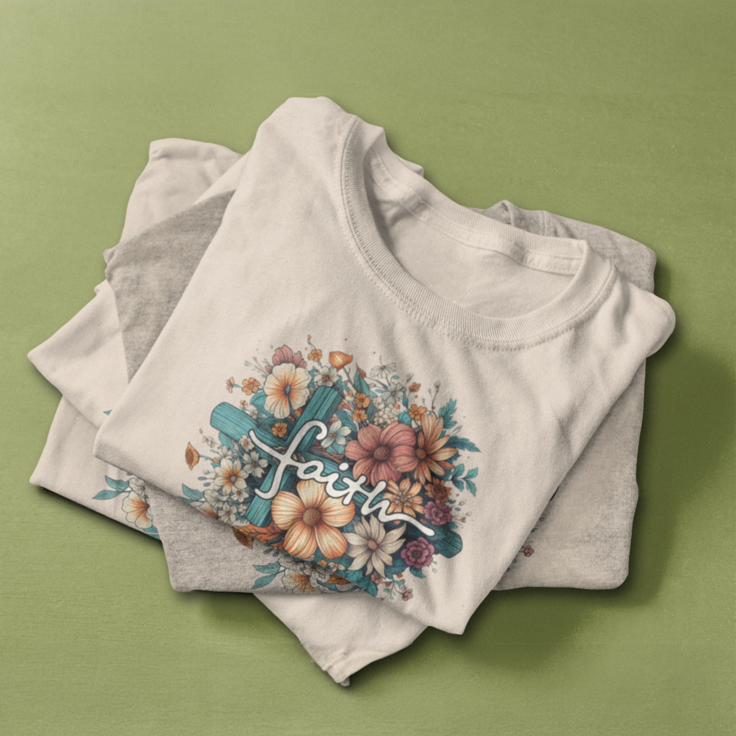 Flat lay of a beige t-shirt featuring a floral design with soft pastel flowers, a cross, and elegant script reading "Faith."