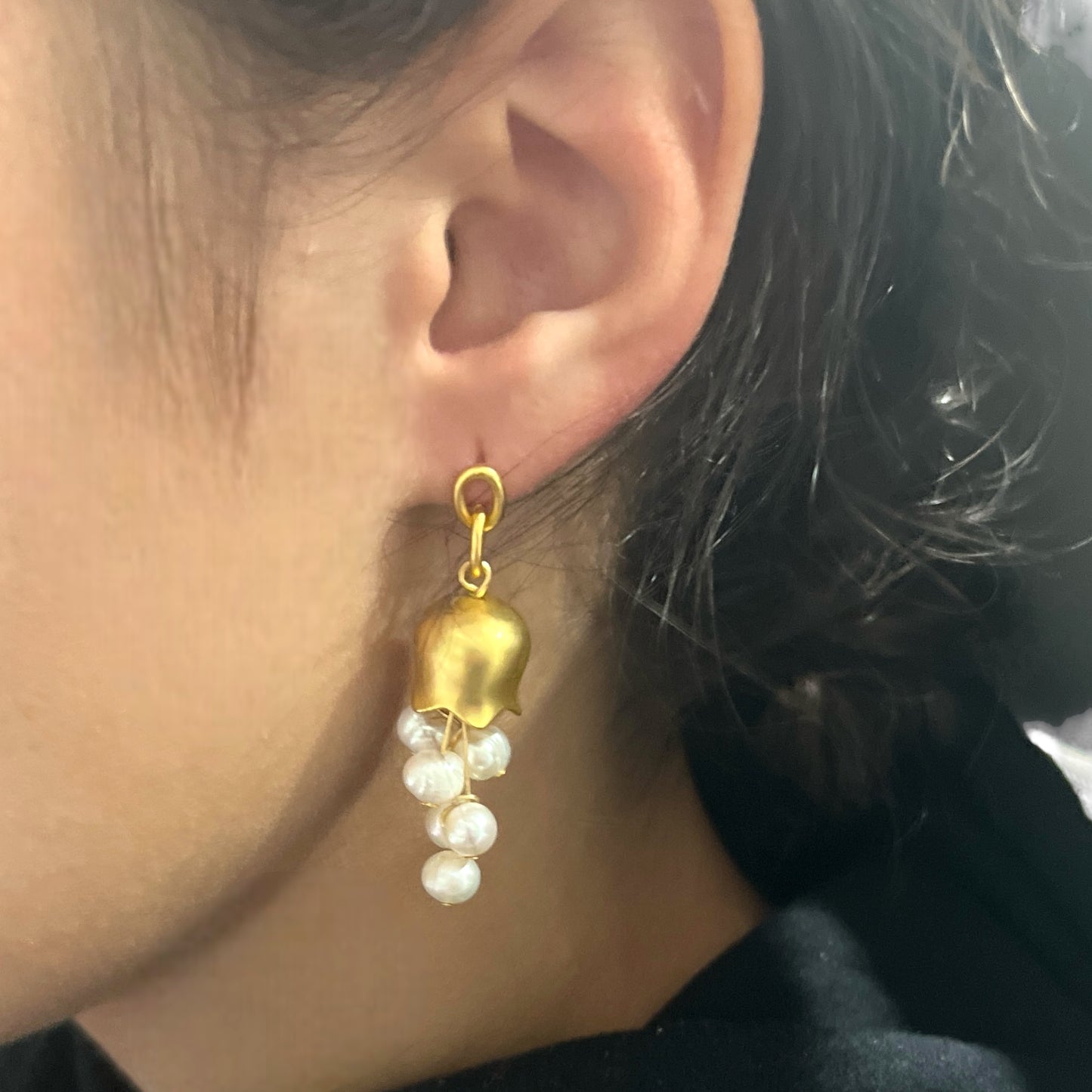 Gold bellflower pearl earrings elegantly worn, showcasing their floral bell shape and cascading pearl accents for a chic statement.