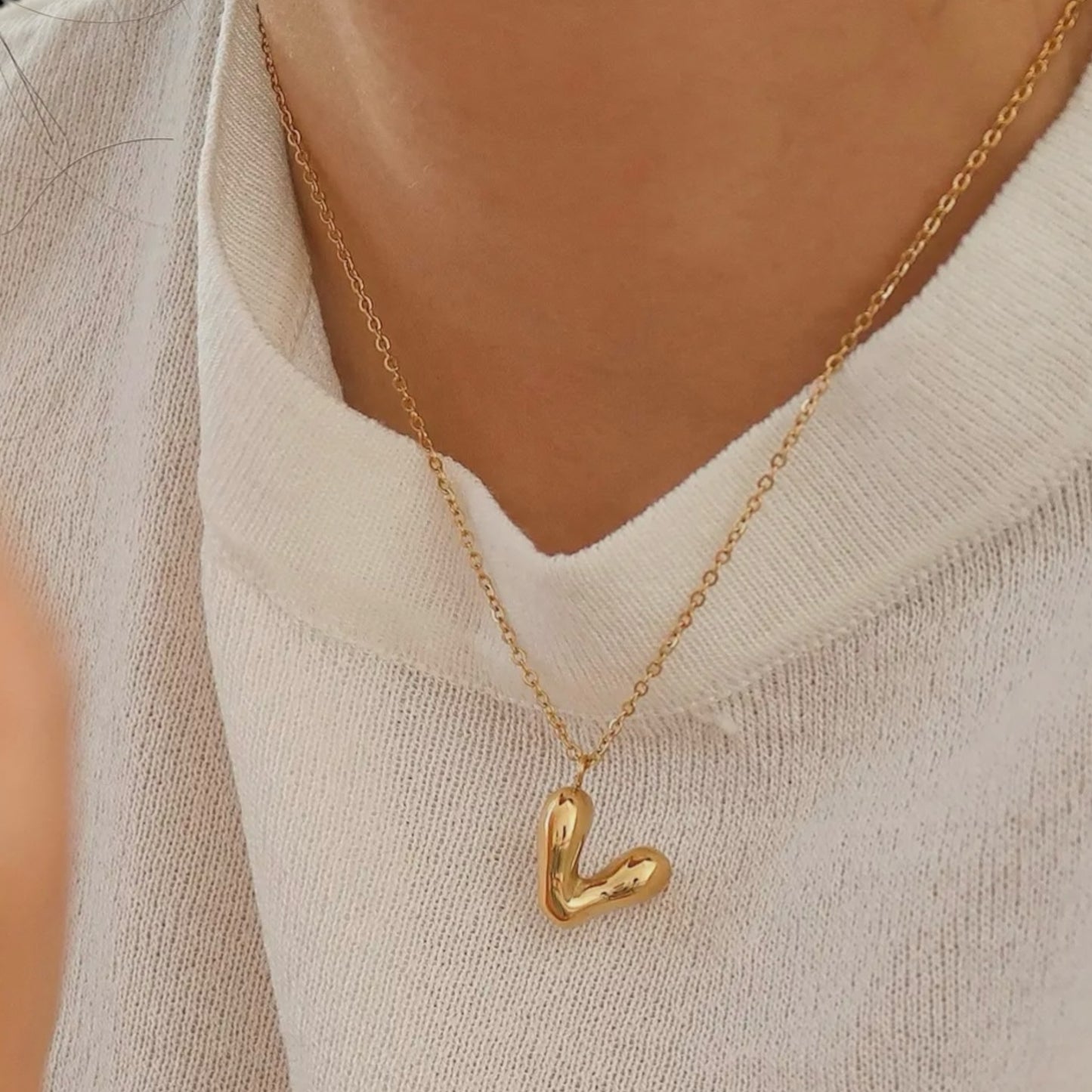 Stylish gold necklace with a puffy V heart pendant shown worn against a white top, highlighting its simple yet sophisticated design.