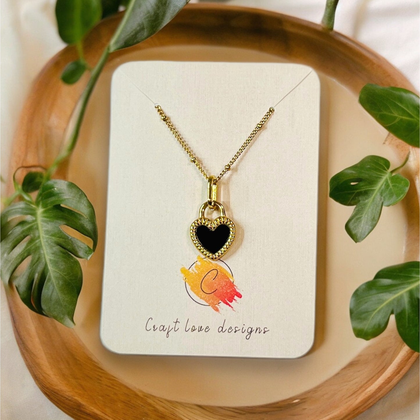 Gold heart pendant necklace with a reversible black and white design, elegantly displayed on a branded jewelry card with plant accents.
