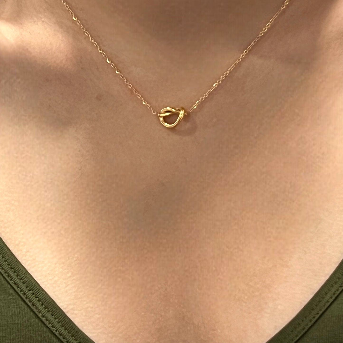 Minimal gold knot pendant necklace worn by a model, showing its elegant fit against a neutral green top.