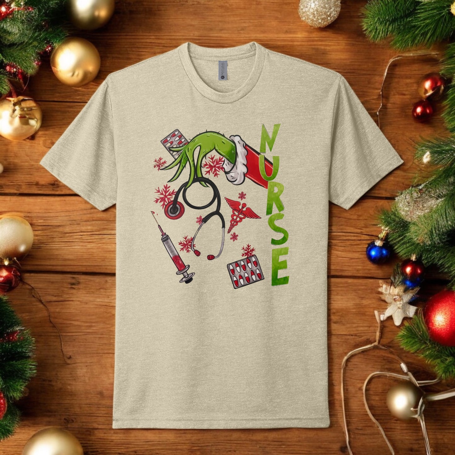 Flat lay of a beige Grinch-themed nurse t-shirt featuring holiday medical graphics like stethoscopes, syringes, and festive decor.