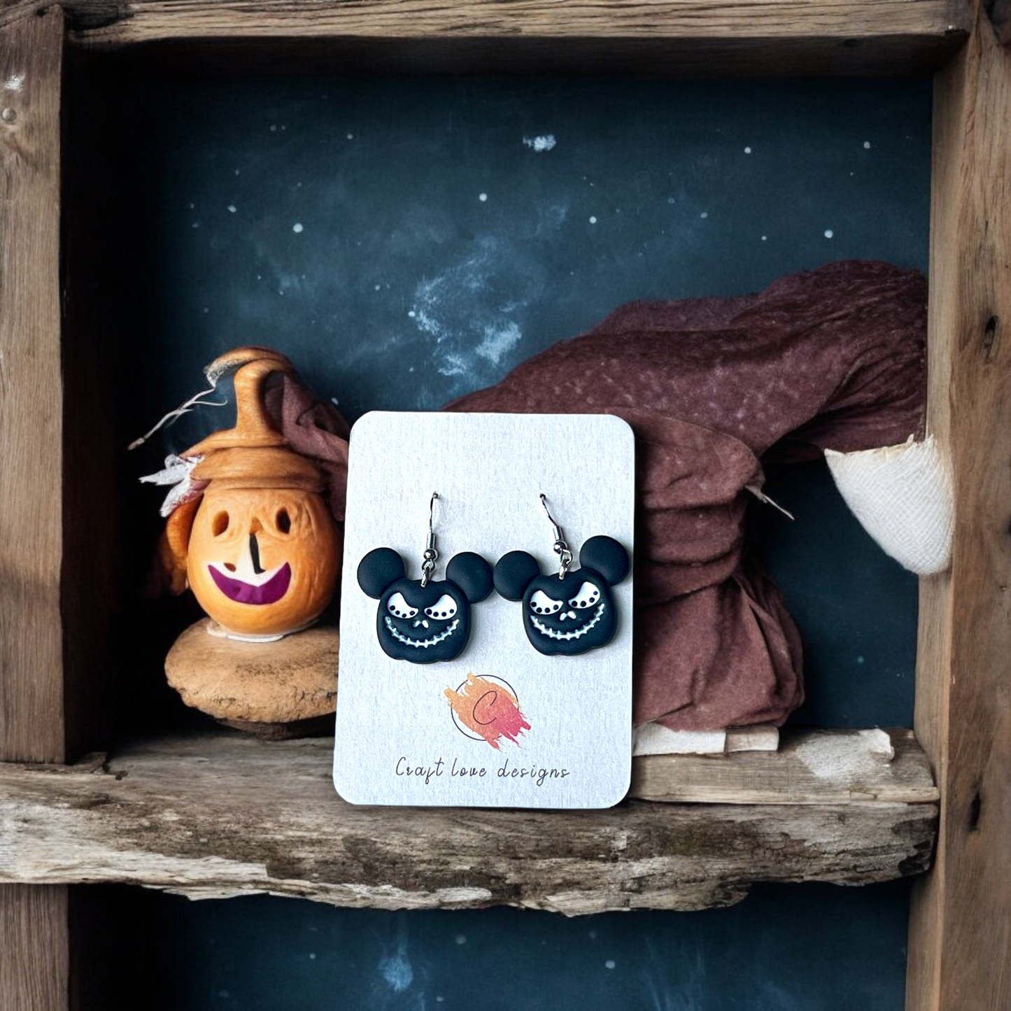Mickey-shaped black Halloween earrings with a creepy smile, presented on a display card inside a rustic wooden frame with spooky decorations.