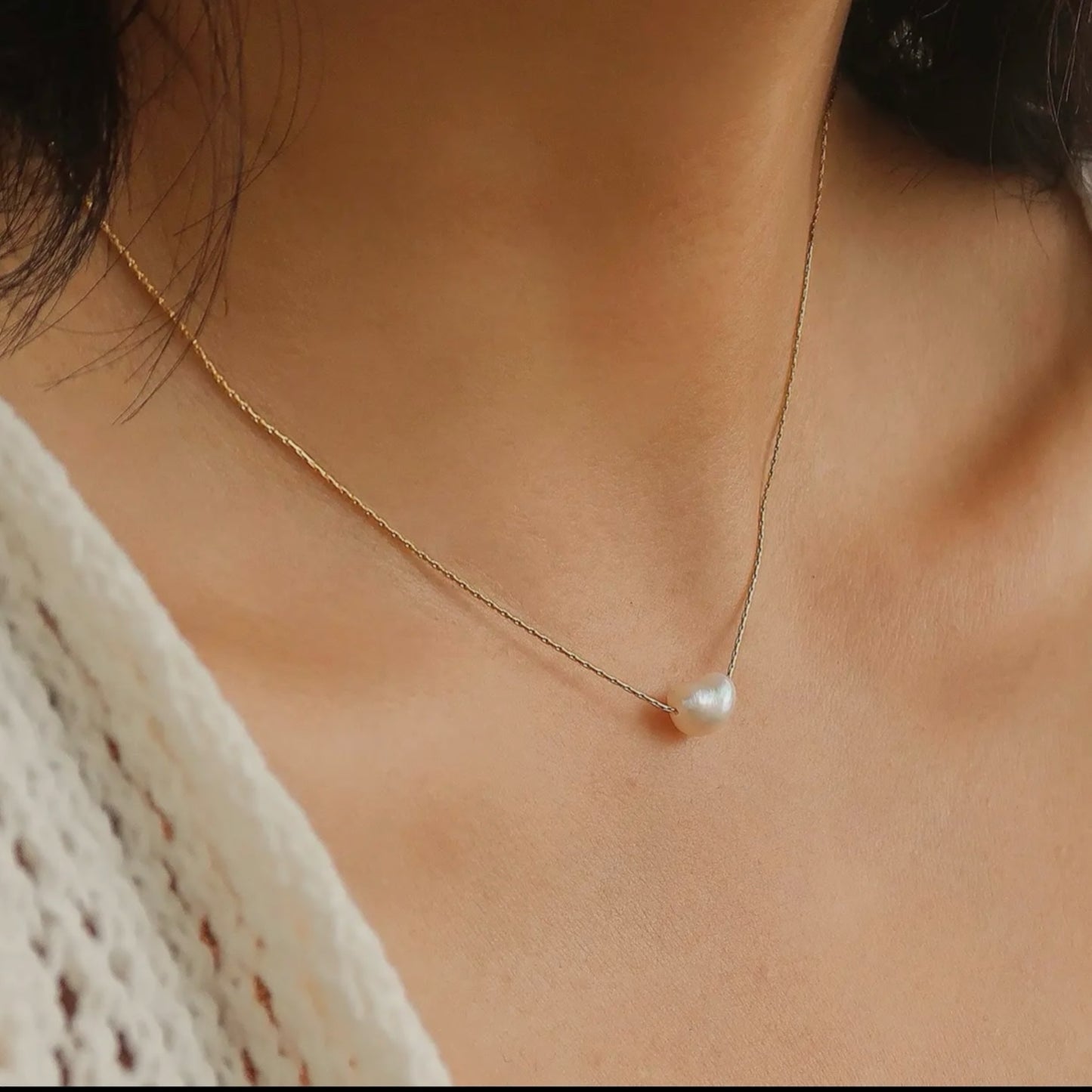 A natural pearl necklace gracefully worn, resting gently on the collarbone, emphasizing its simplicity and sophistication on a gold chain
