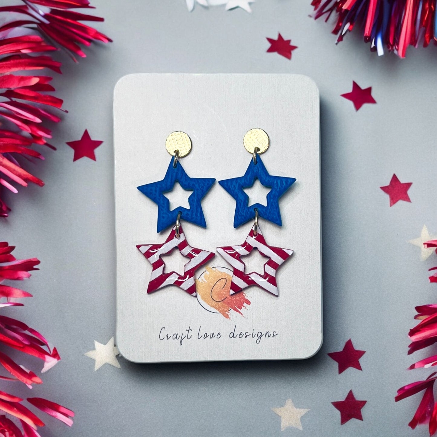 Festive red and blue polymer clay star dangle earrings with gold accents, perfect for adding a bold touch to 4th of July outfits.