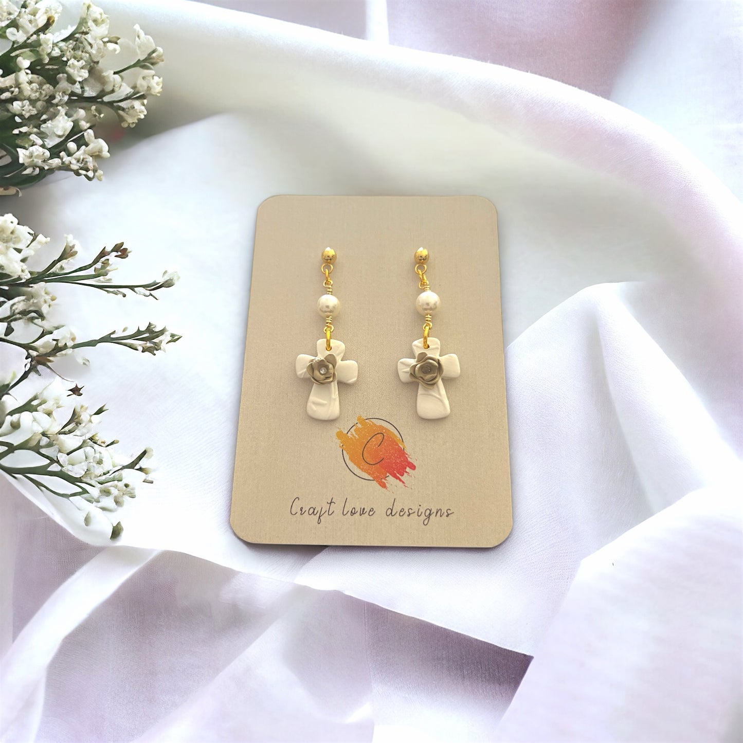 Pearl drop dangle earrings with a textured cross charm adorned with floral accents, displayed on a card with a minimal and elegant backdrop.