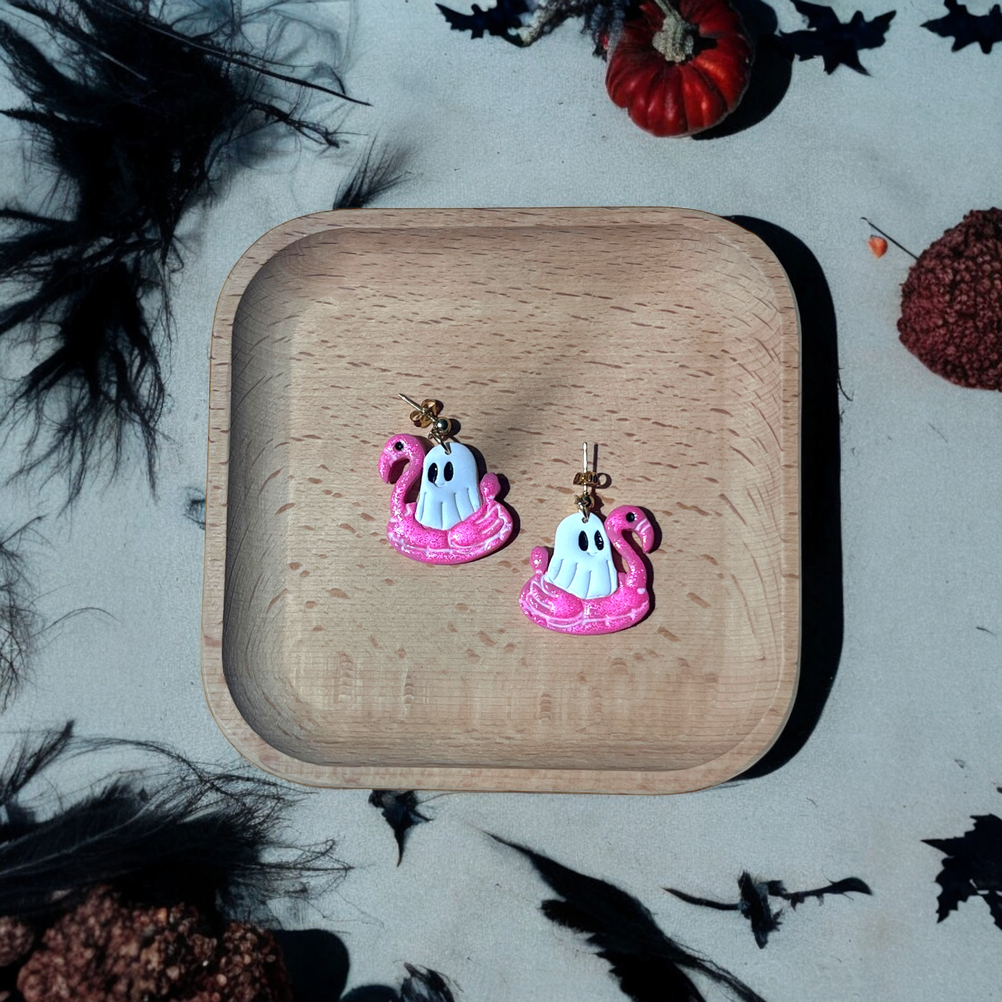 Whimsical ghost earrings sitting in glittery pink flamingo floats, a fun mix of tropical and Halloween vibes for a unique accessory.
