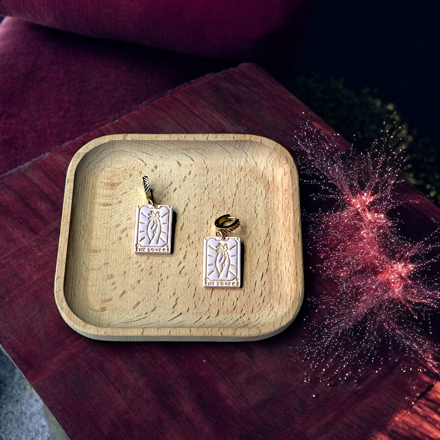 Pastel pink tarot card drop earrings with gold hooks and embossed "The Lovers" detailing, placed on a wooden tray with a cosmic fabric backdrop.