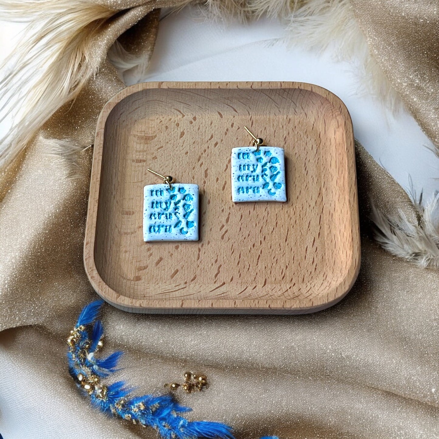 Fun and vibrant 'In My Eras Era' earrings displayed on a wooden plate with light blue icons and sparkling details.