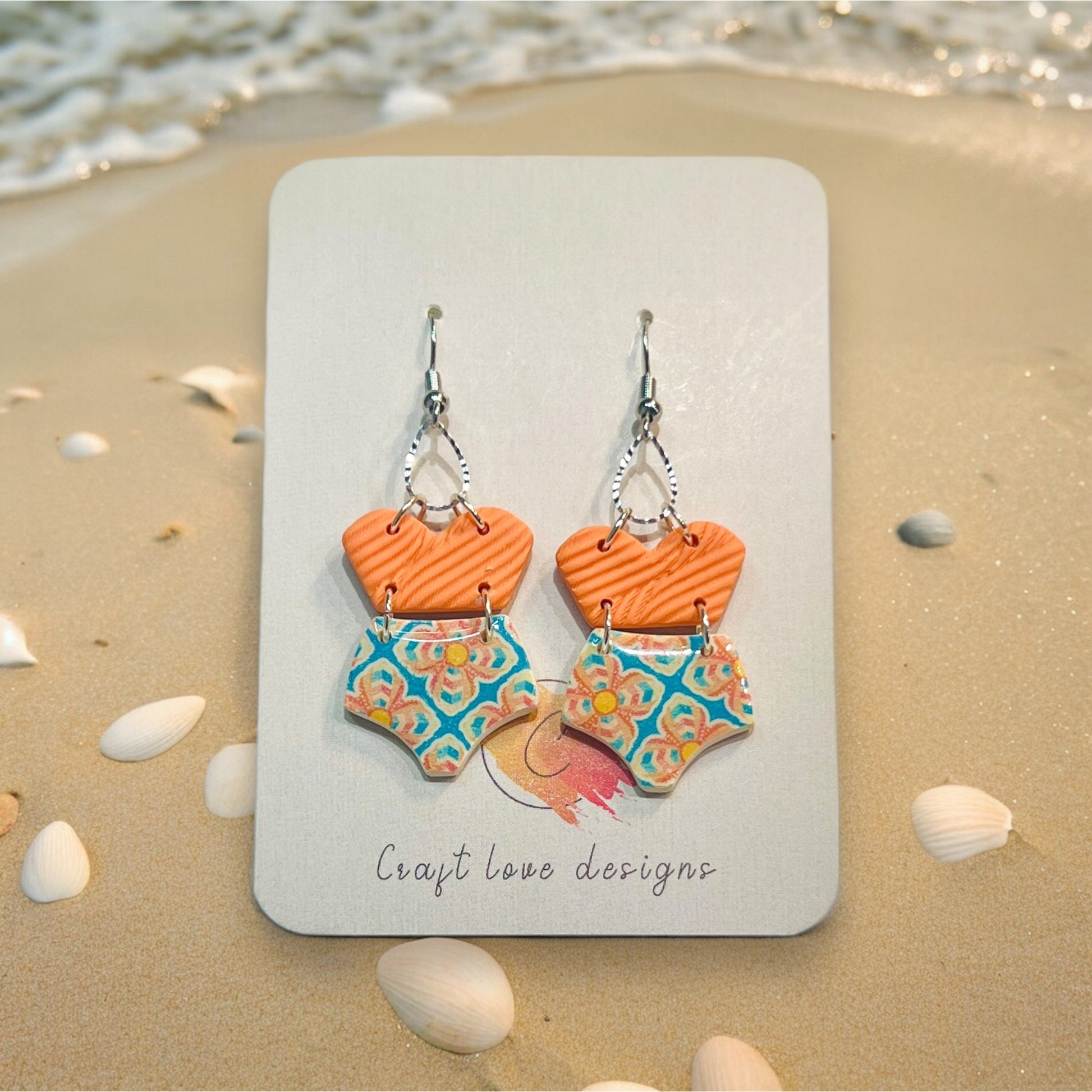 Close-up of playful polymer clay earrings with swimsuit shapes, featuring orange tops and patterned bottoms, perfect for beach vibes.
