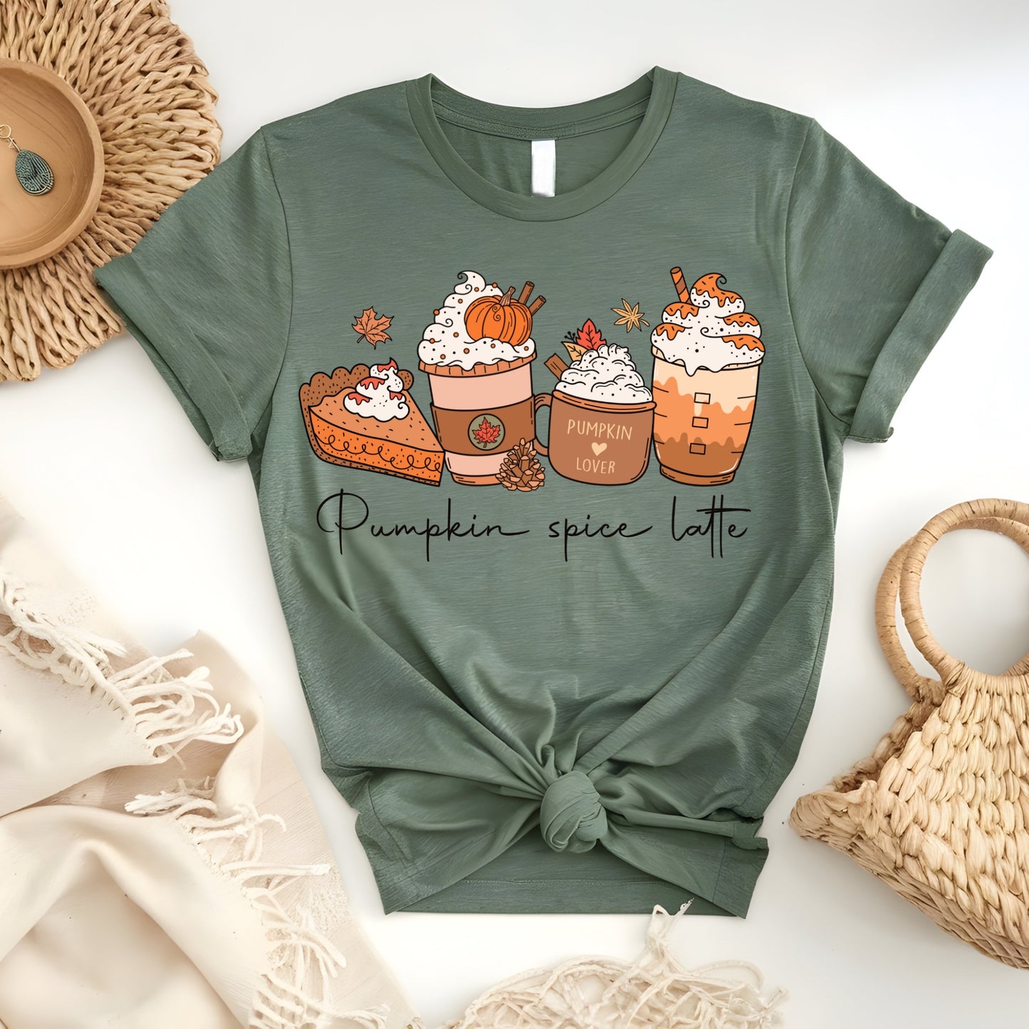 Flat lay of a sage green t-shirt featuring cute illustrated pumpkin spice lattes, autumn leaves, and hand-drawn text, perfect for fall.design.