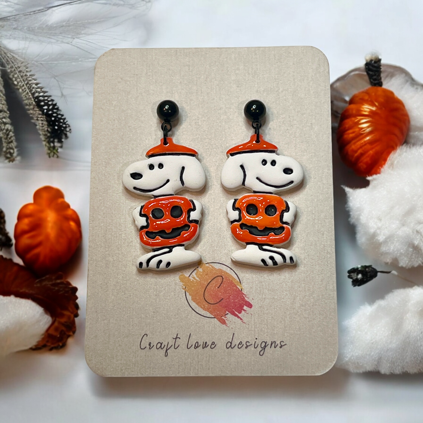 Cute polymer clay earrings featuring a white dog wearing an orange pumpkin costume and hat, perfect for fall and Halloween outfits.