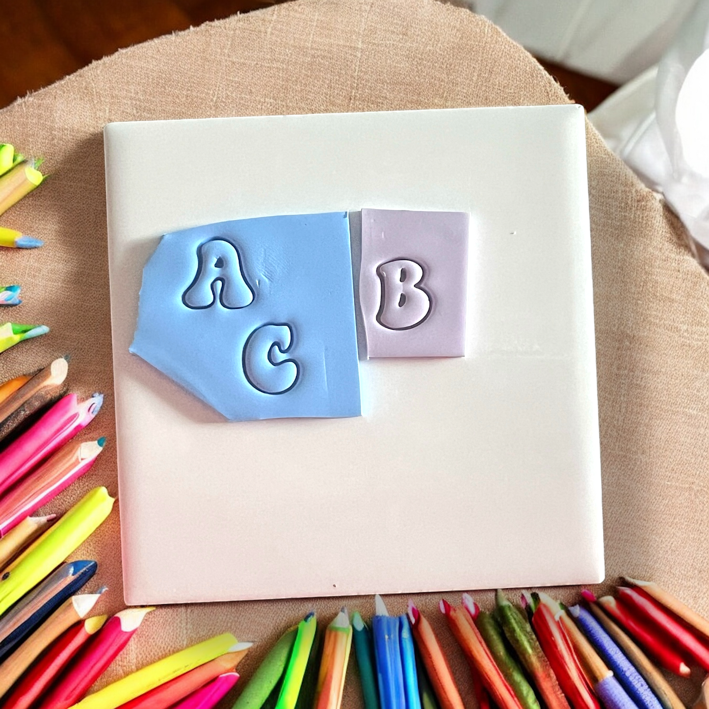 Letter-shaped stamps on a white block with colorful pencils around