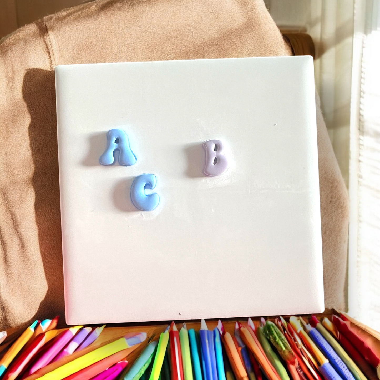 White board with colorful letters 'A', 'B', and 'C' on a beige surface with colored pencils below.