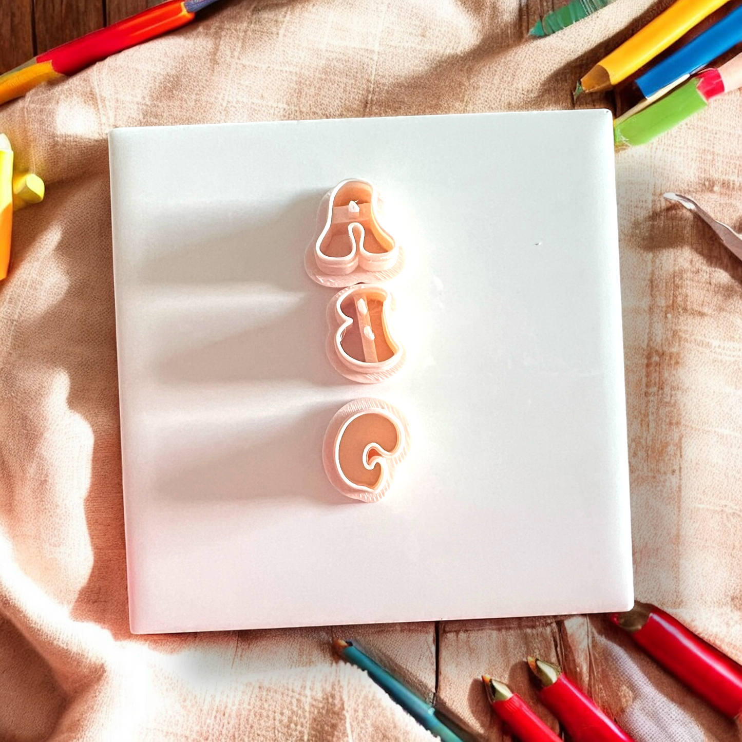 Two letter 'A' and 'G' cookie cutters on a white sheet of paper with colorful pencils around.