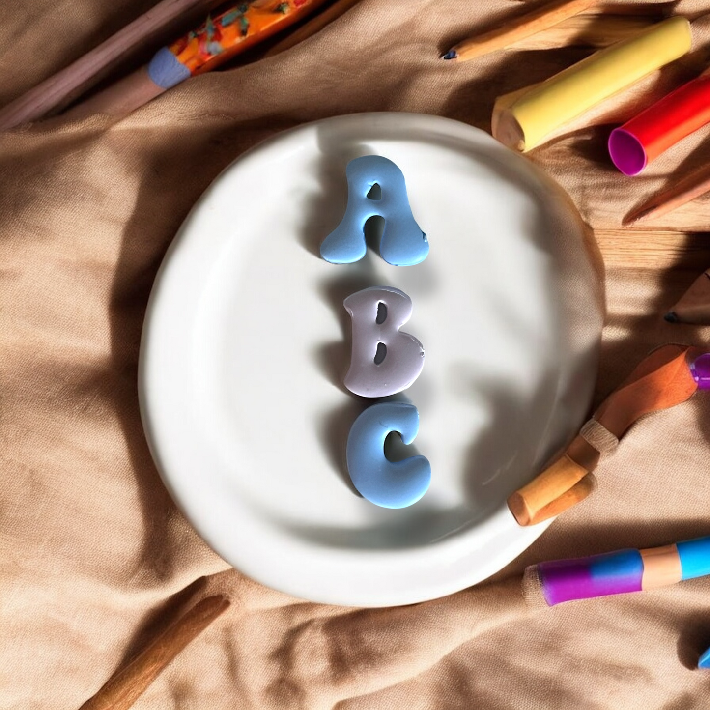 White ceramic plate with 'ABC' letters surrounded by colorful crayons on a wooden surface