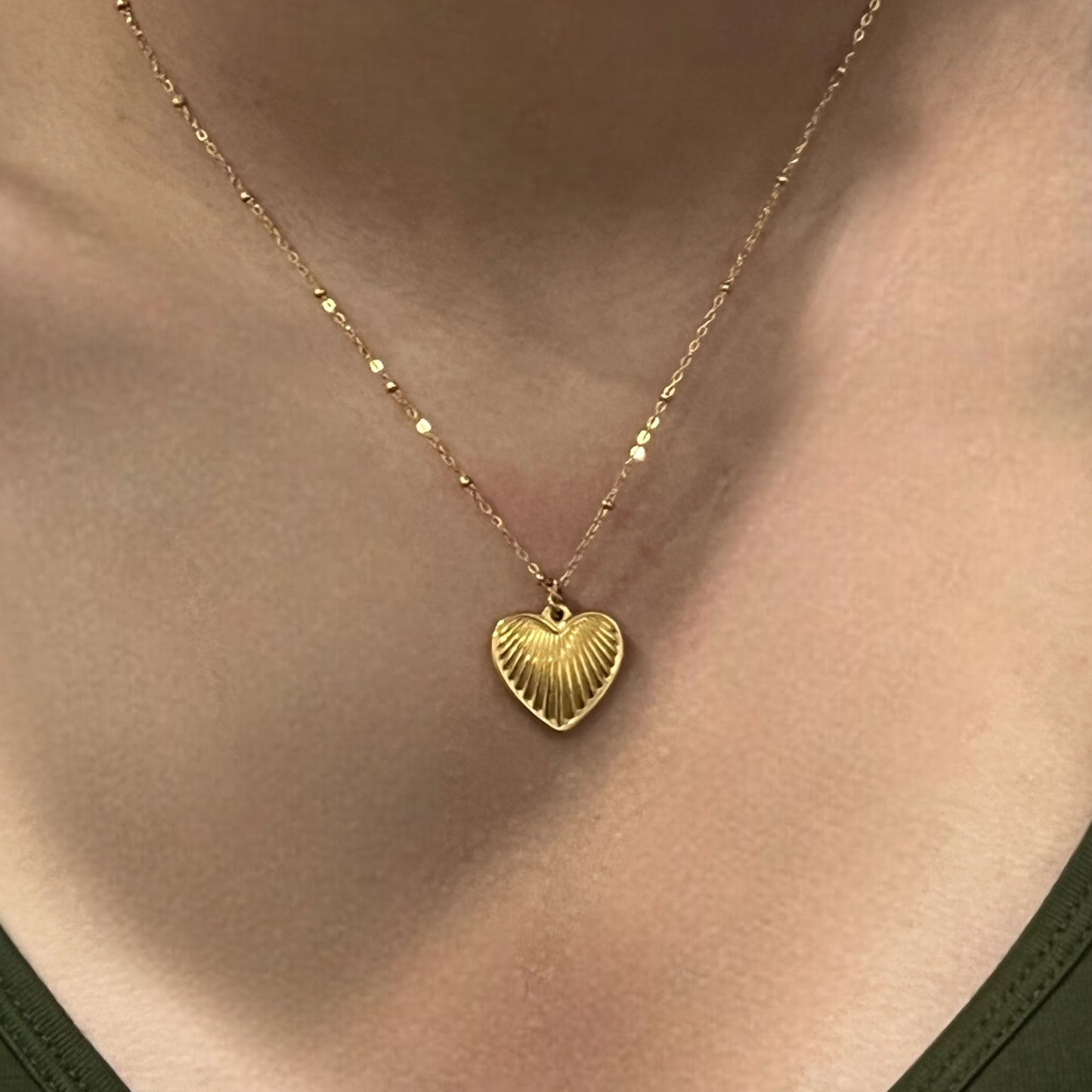 Close-up view of the ribbed gold heart pendant necklace resting against the neck, offering a timeless touch for elegant or casual outfits.