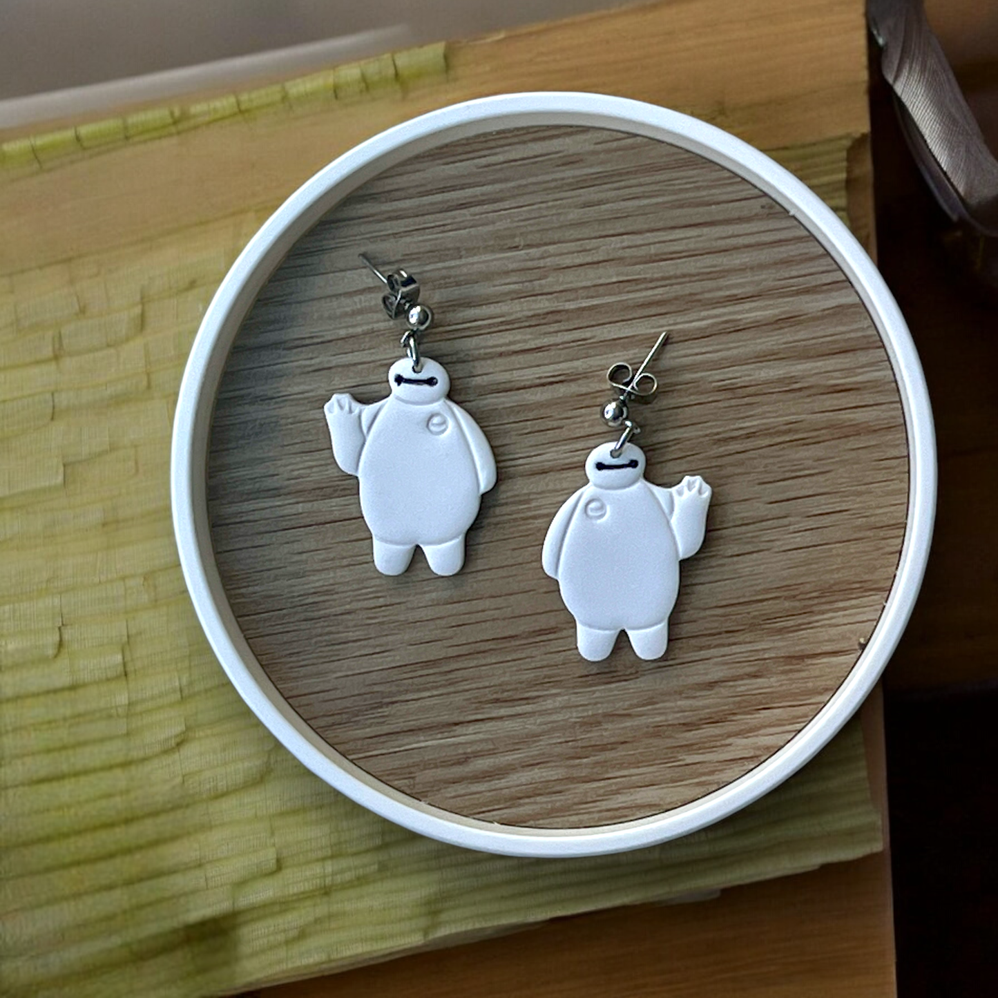 Robot character-themed polymer clay dangle earrings with waving design, placed on a round wooden tray for display.