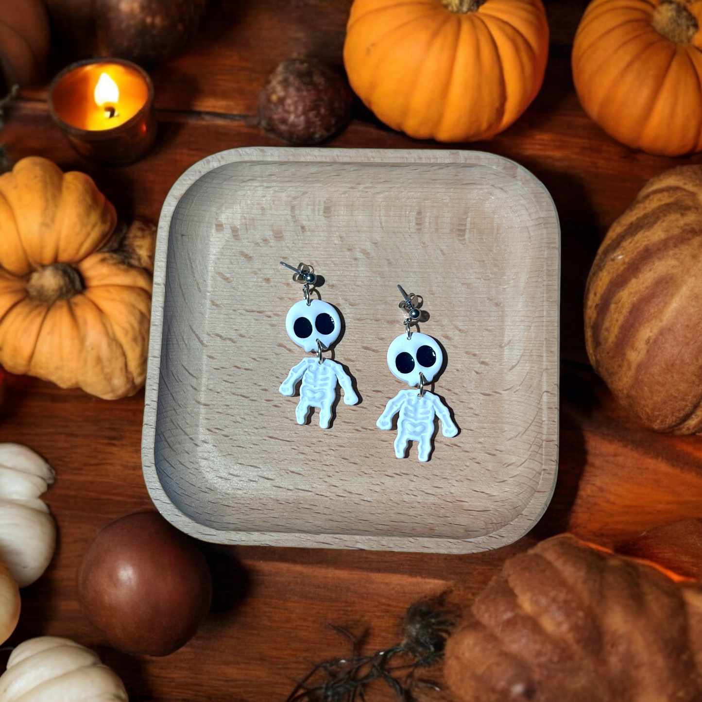 Black and white skeleton cameo earrings resting in a wooden tray, surrounded by decorative pumpkins for a spooky, fall-inspired look.