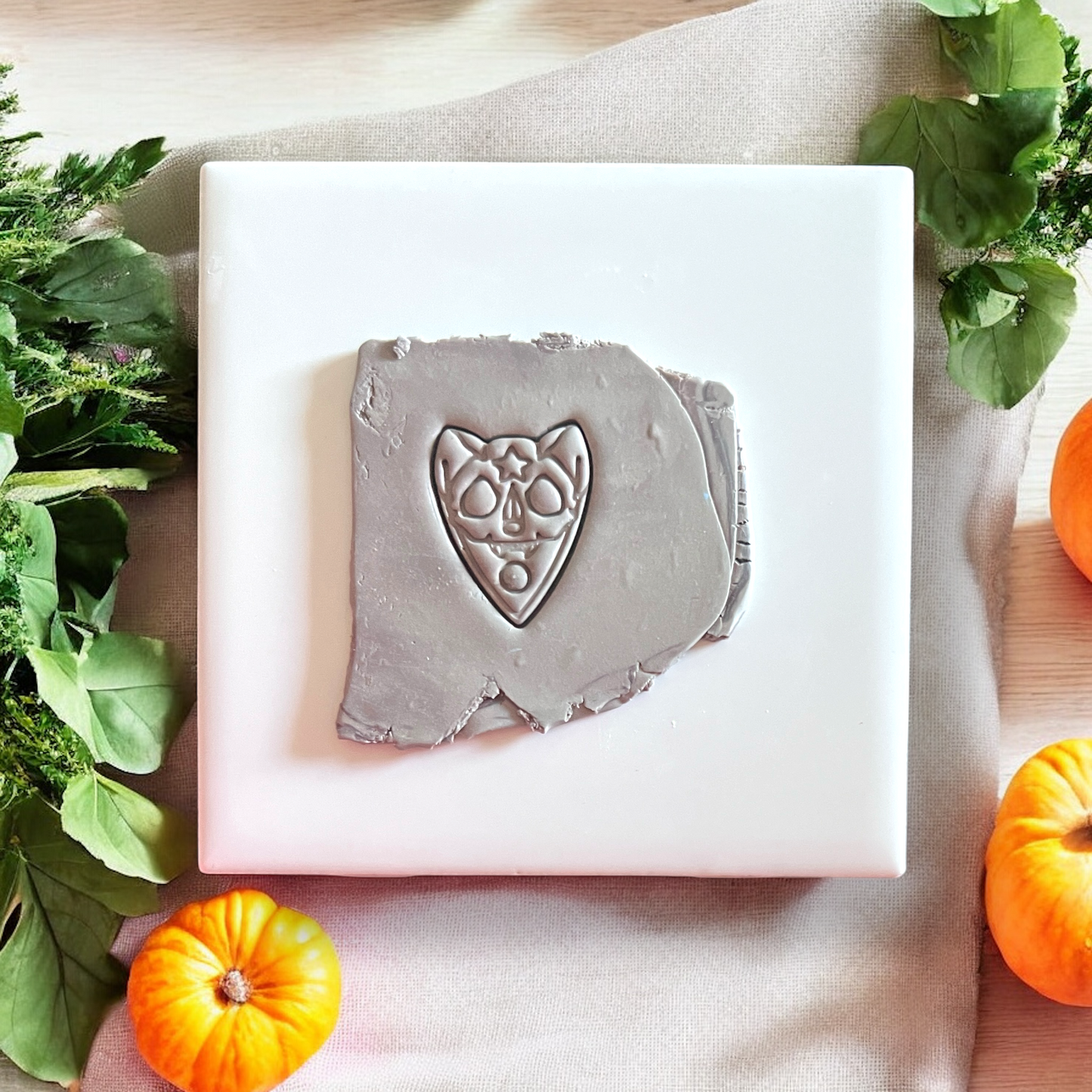 Embossed sugar skull cat design impressed in gray clay on white tile