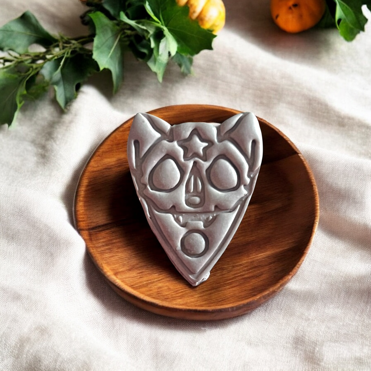 Close-up of finished clay earring piece on wood dish with pumpkins