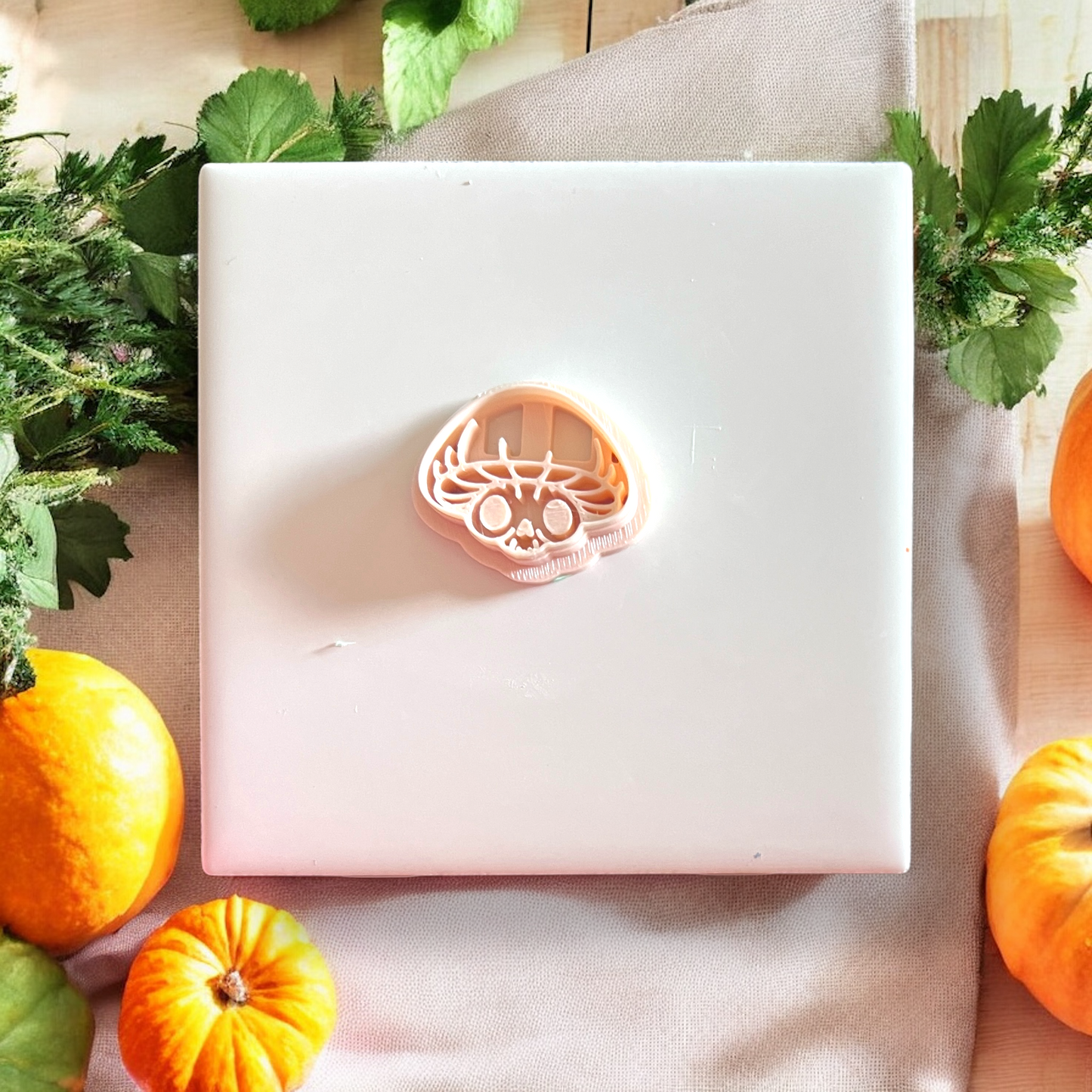 Mushroom skull clay cutout centered on white tile with scattered pumpkins and leaf shadows