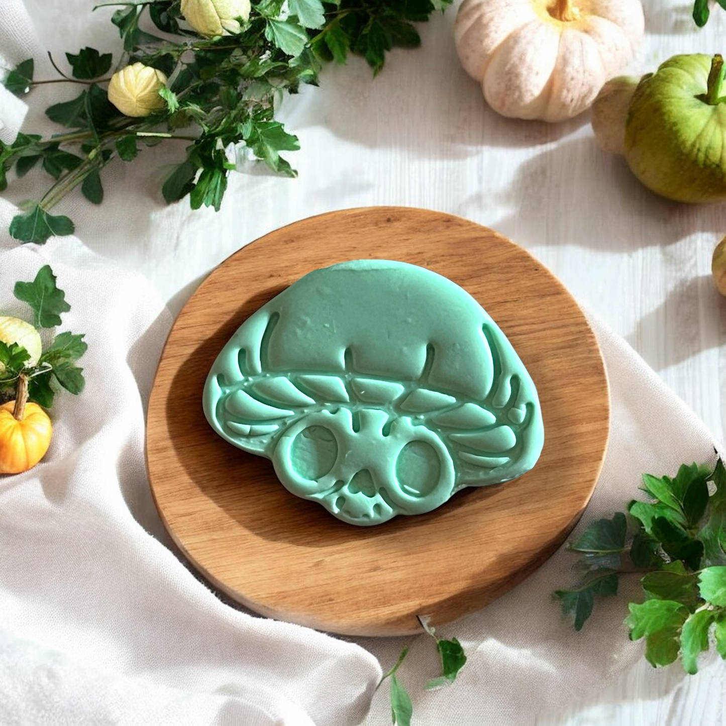 Orange mushroom skull cutter on tile next to finished mint green clay version, surrounded by greenery