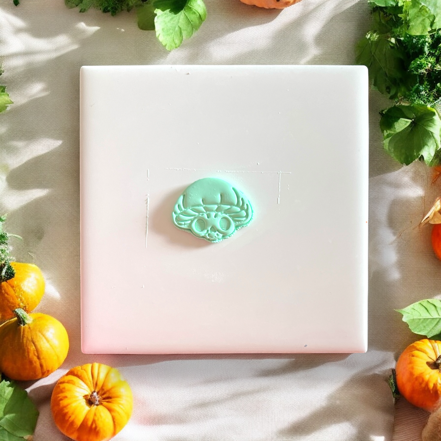 Cut clay piece shaped like a mushroom with a skull face, surrounded by fall leaves and pumpkins
