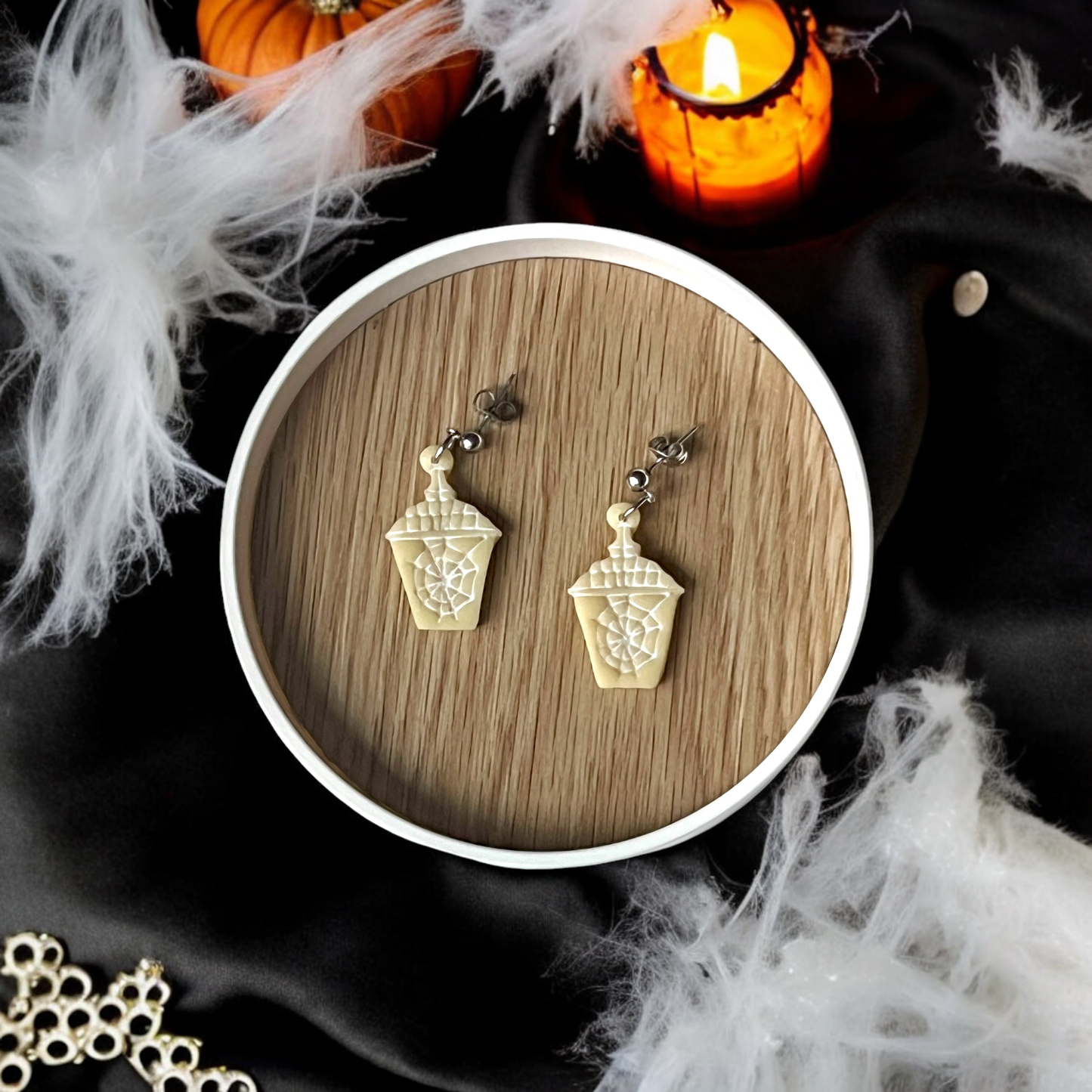 Halloween-themed coffee cup earrings with a spider web design, placed on a wooden tray with glowing candles, cobwebs, and spooky decor.