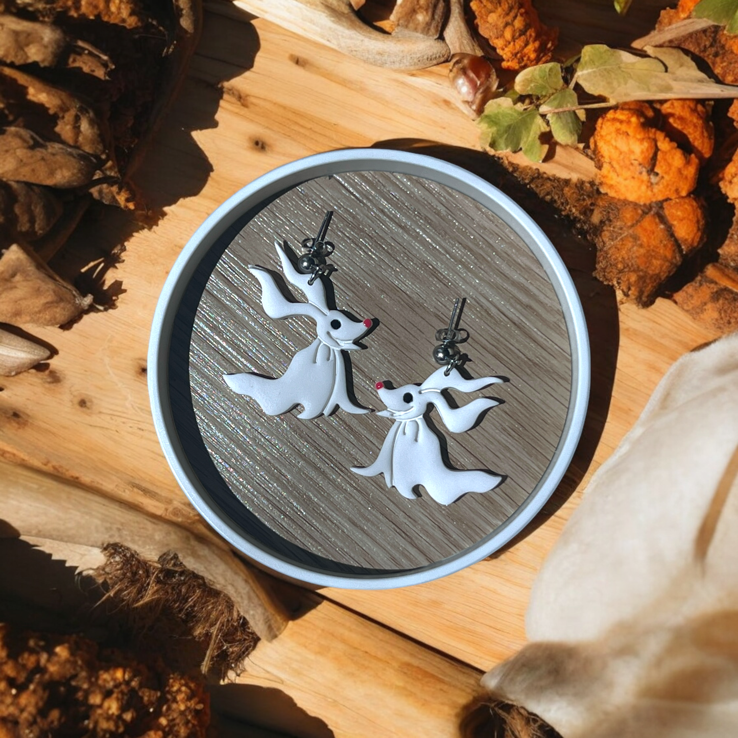 Ghost dog earrings with floppy ears and cute red noses displayed on a decorative wooden plate with autumn-inspired surroundings.